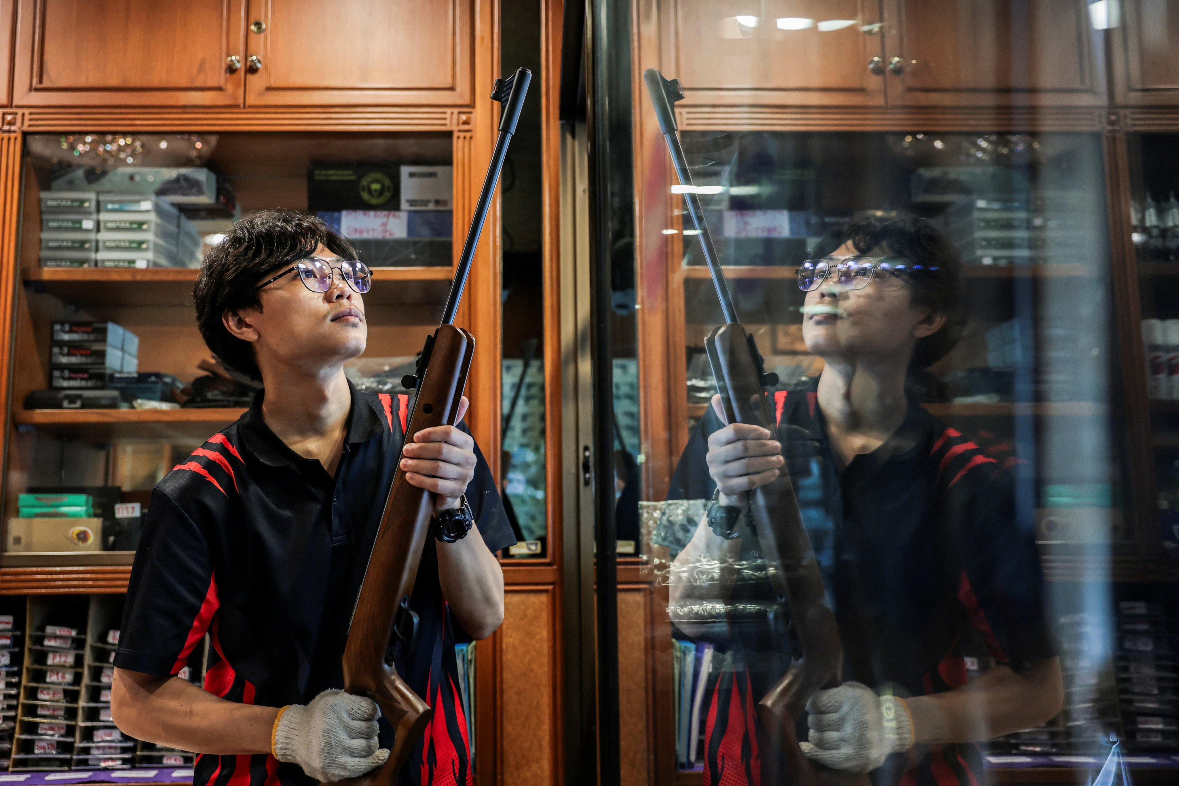 Gun shop worker Piyawat Lumlertwittaya places a rifle  back on a display shelf on Friday. Photo: Reuters