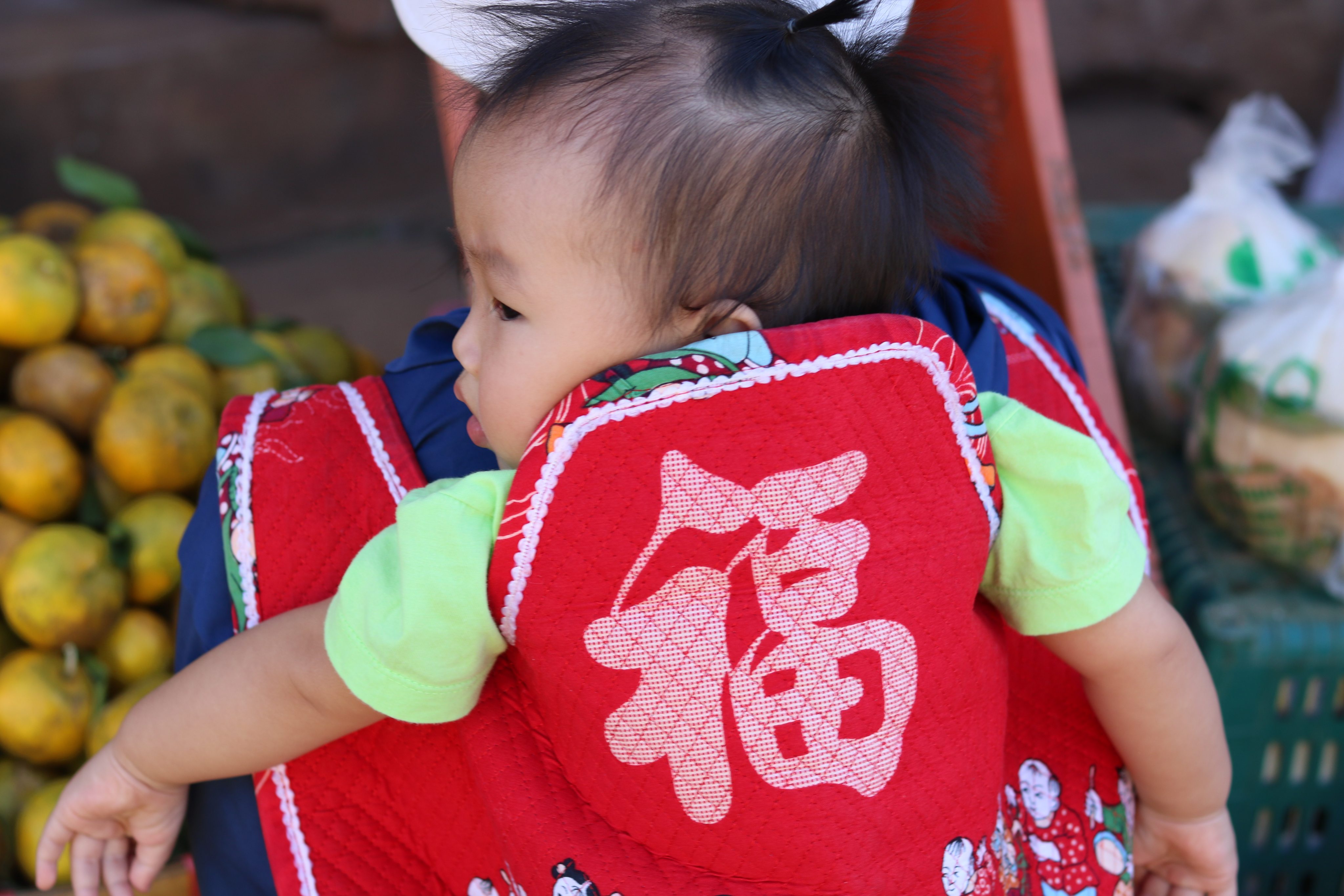 A baby in a back sling adorned with Chinese character meaning “fortune” in Ban Arunothai, Thailand. Photo: Thomas Bird