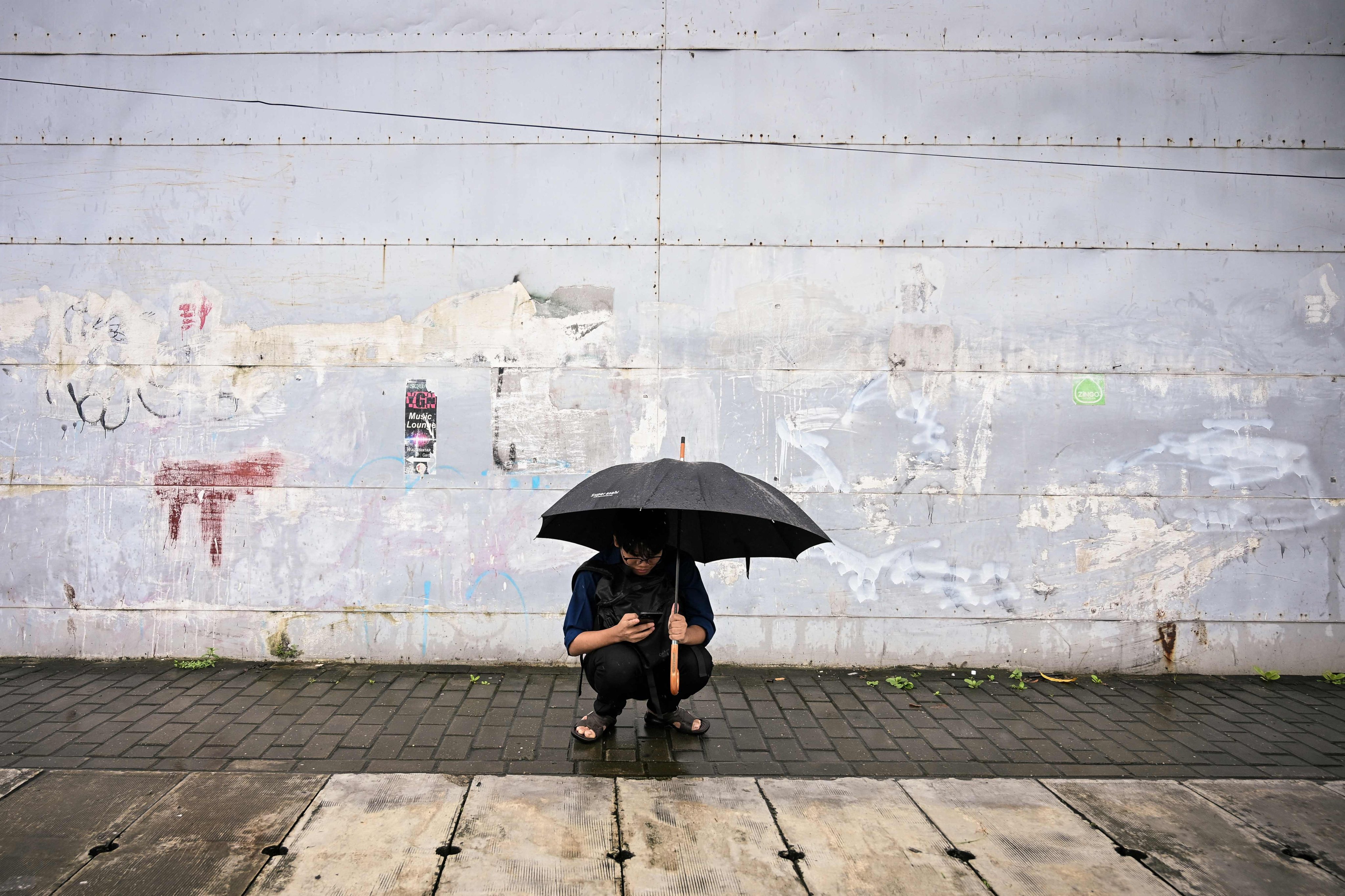 A man uses his mobile phone while sheltering under an umbrella as rain falls in Yangon, Myanmar, on August 11. Photo: AFP