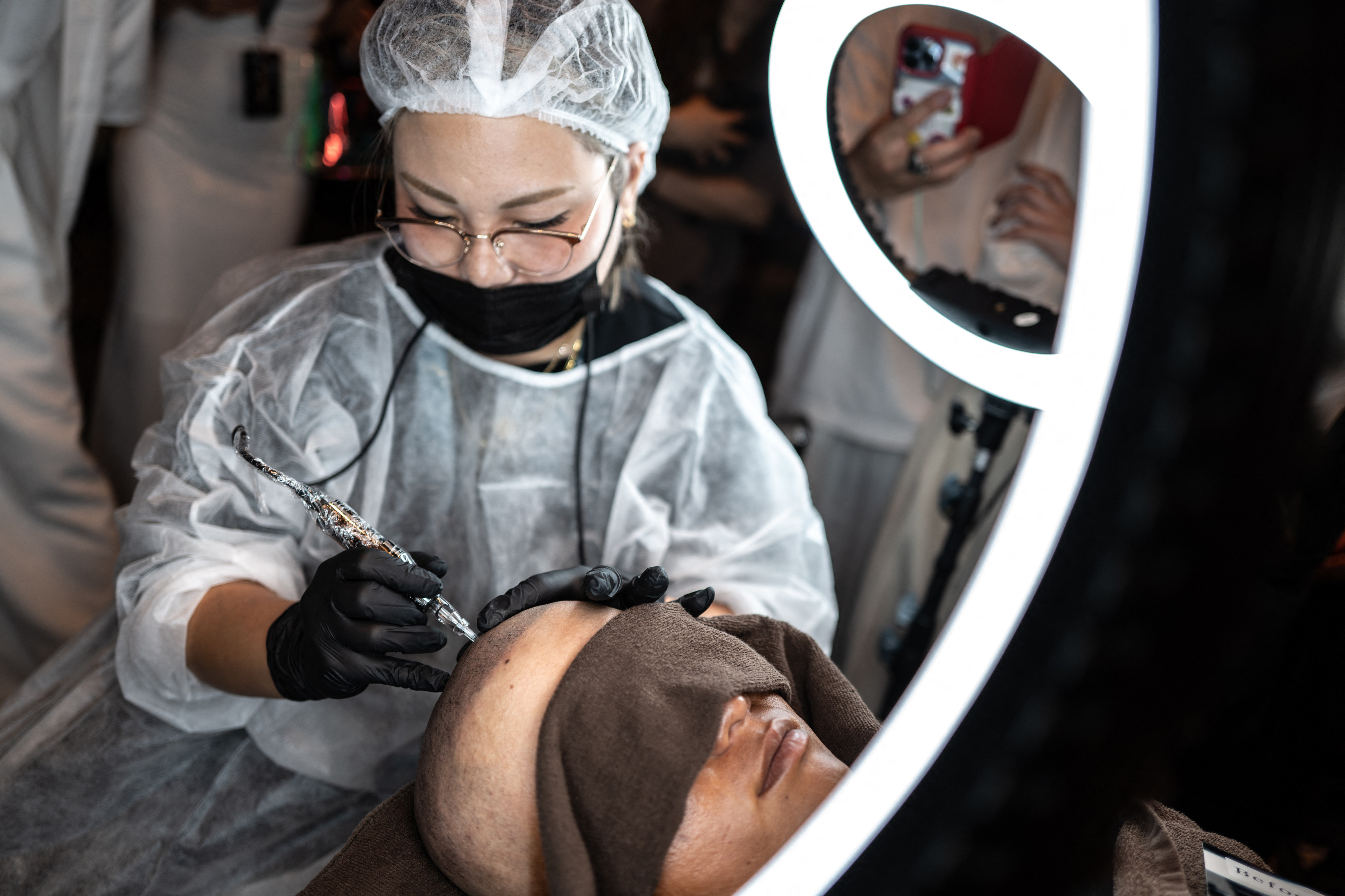 This picture taken on July 8, 2026 shows a scalp tattoo artist conducting a demonstration during a tattoo and permanent make up contest in Naha, Okinawa Prefecture. Japan bucks a global trend by viewing permanent make-up as the domain of medical professionals, and has ramped up threats of criminal prosecution against anyone else who practises it. Industry insiders insist that their craft, from make-believe hair to filled-in eyebrows and lip tints, is an artistic pursuit more befitting tattooists and hairstylists. But in a country where body art has long symbolised yakuza gangsters, these cosmetic tattooists’ safety and sanitary protocols are not enough to dispel scepticism. (Photo by Philip FONG / AFP) / To go with AFP story Japan-tattoo-medicine-cosmetics-society-doctors, FEATURE by Tomohiro Osaki