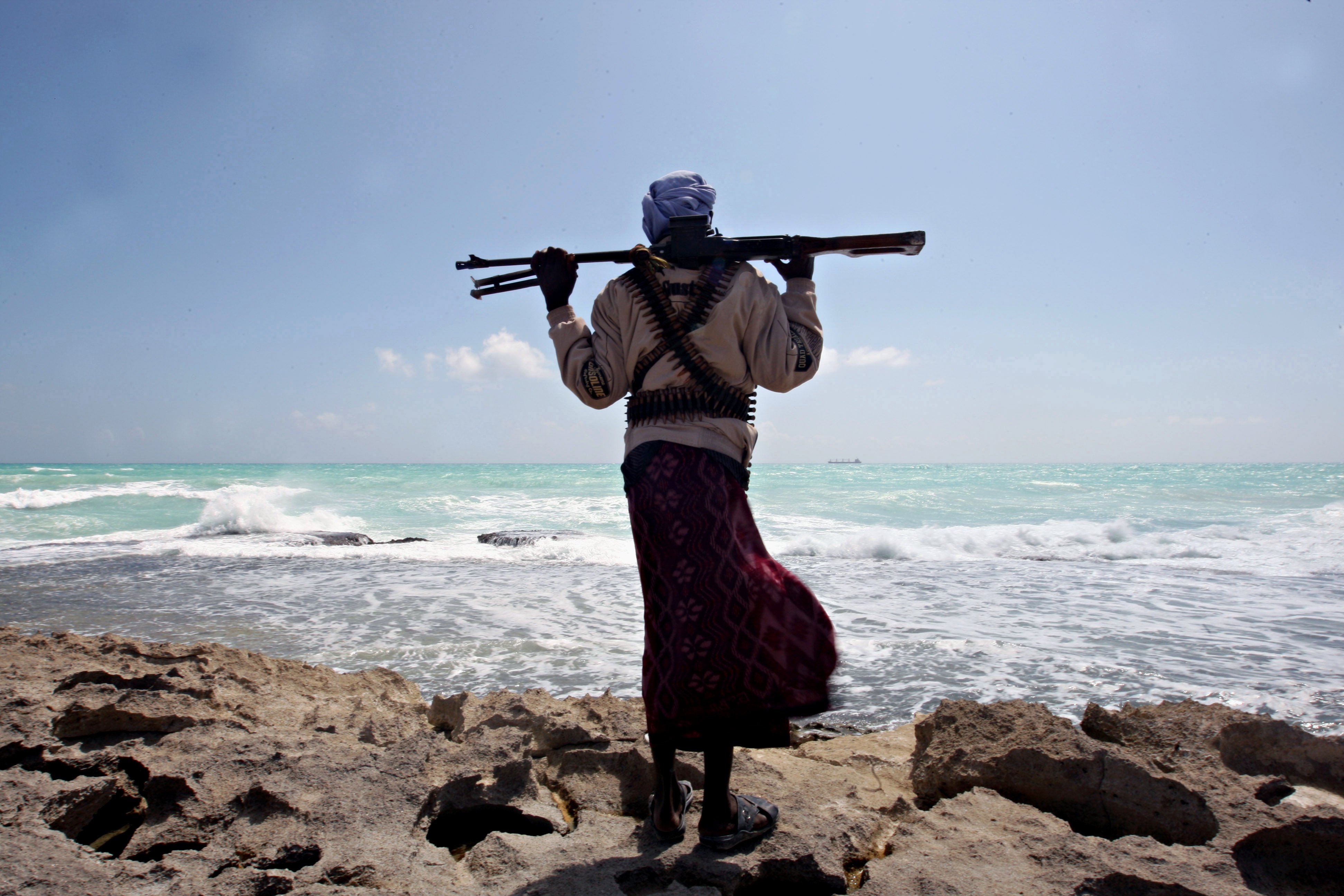 An armed Somali pirate along the coastline while the Greek cargo ship, MV Filitsa, is seen anchored just off the shores of Hobyo town in northeastern Somalia in 2010. Photo: AFP