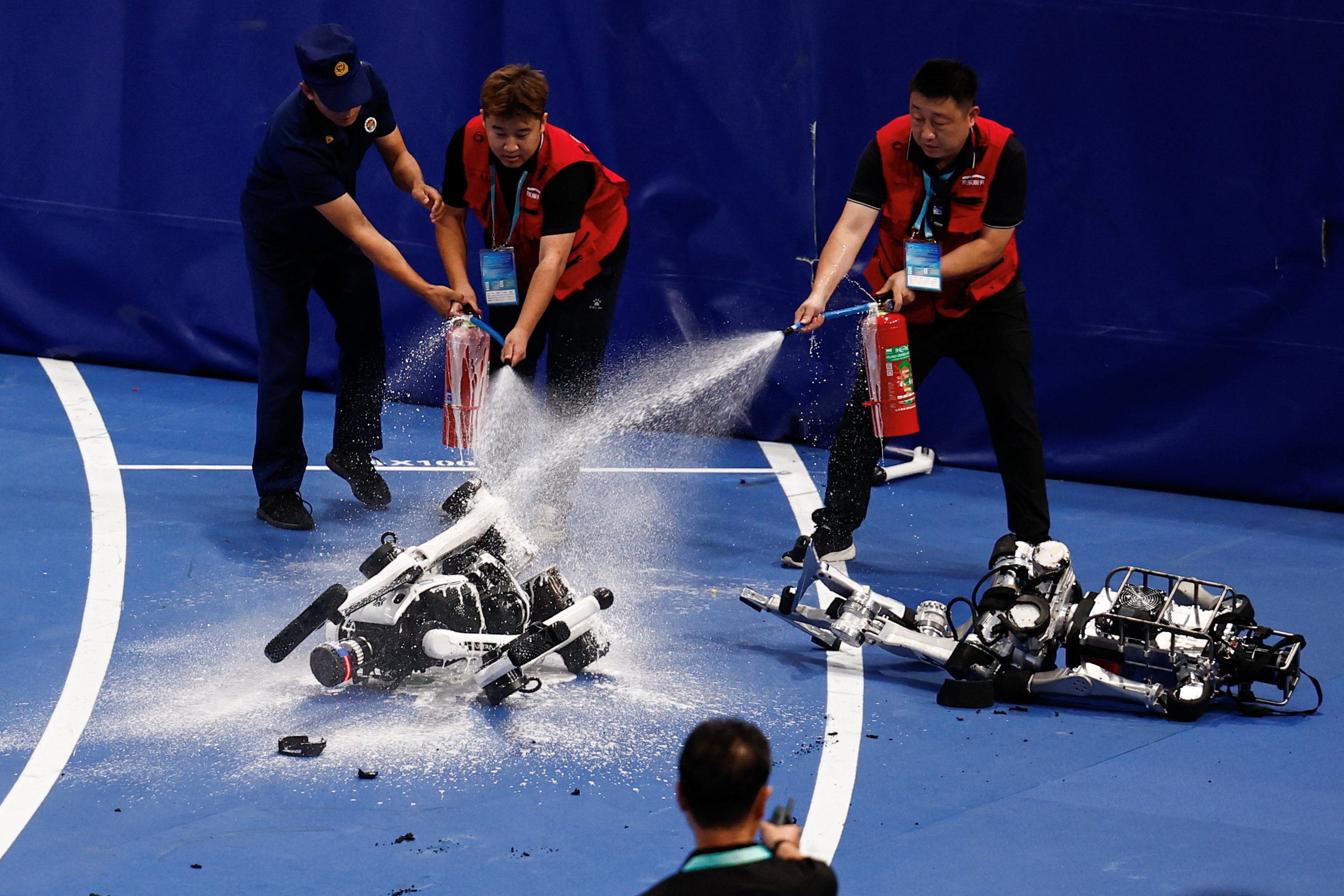 Staff members use extinguishers after a humanoid robot caught fire after finishing a 100m large-sized group preliminary race, following the opening ceremony of the 2026 World Humanoid Robot Games, at the National Speed Skating Oval, in Beijing, China August 22, 2026. REUTERS/Tingshu Wang     TPX IMAGES OF THE DAY