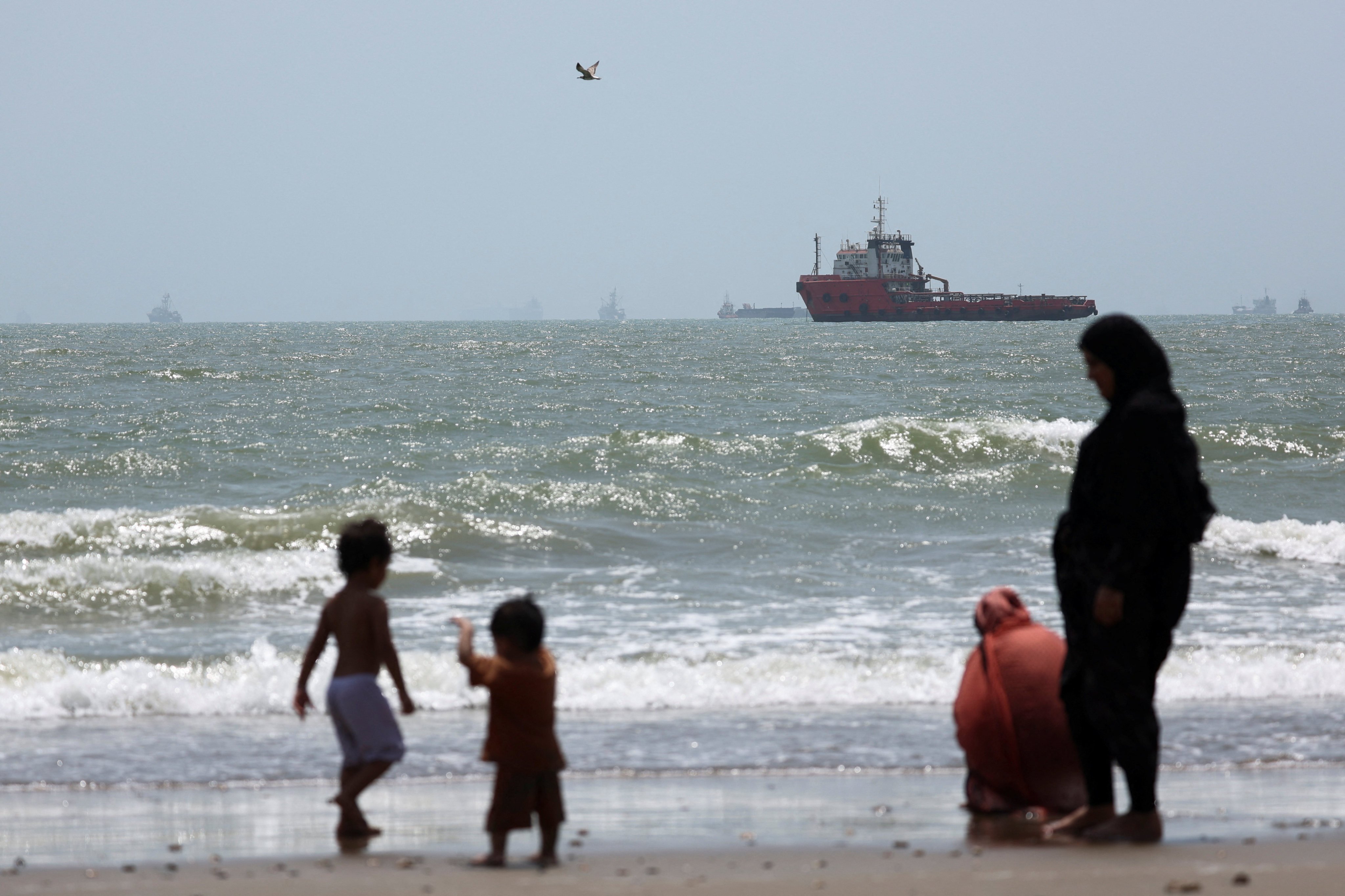 People gather as stranded vessels in the Strait of Hormuz are visible near the beach of Bandar Abbas in Iran on August 25. Photo: Reuters