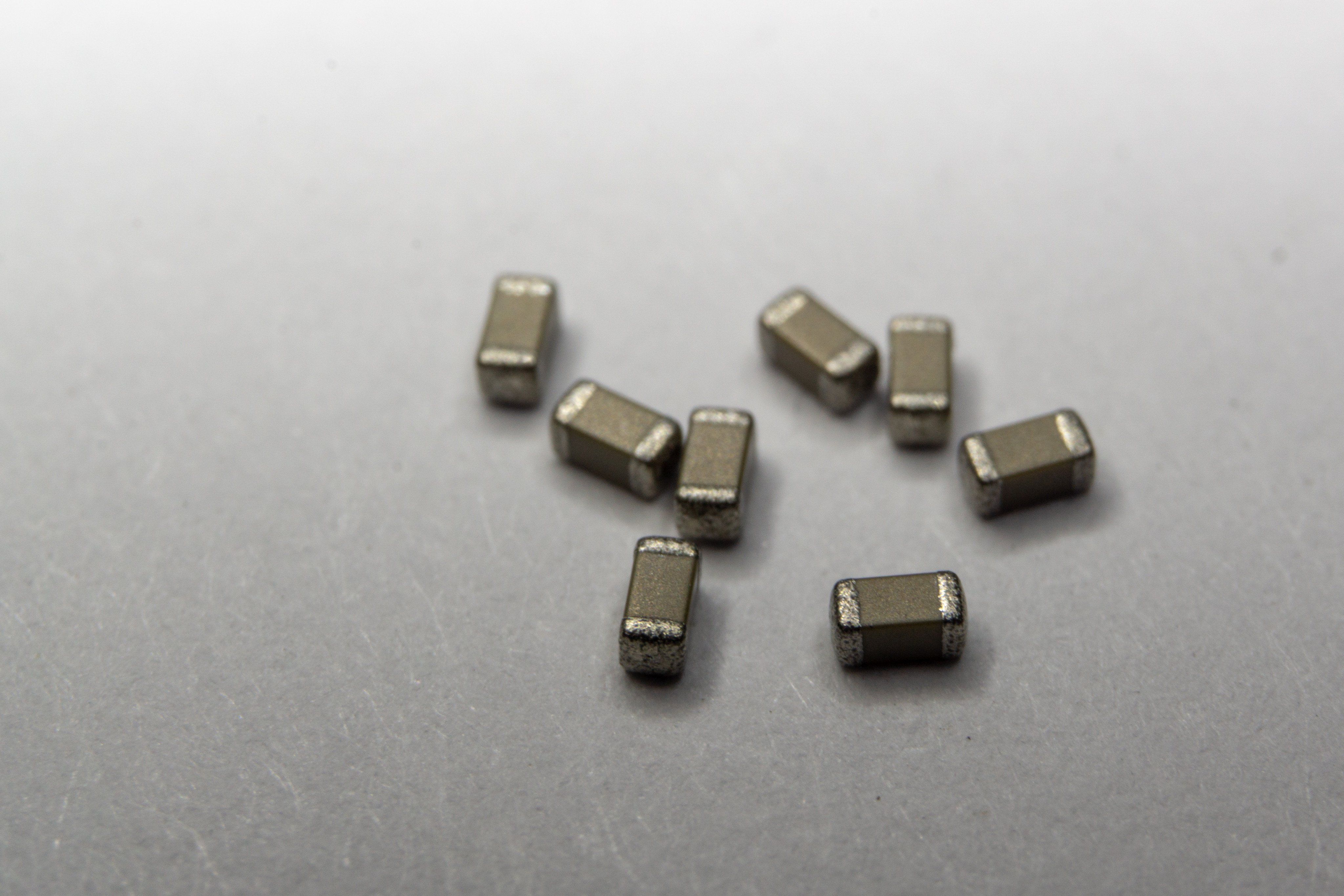 Abstract close-up of grey scattered 0603 SMT surface mount chip MLCC capacitors power electronics components on white background in random pattern. Photo: Shutterstock