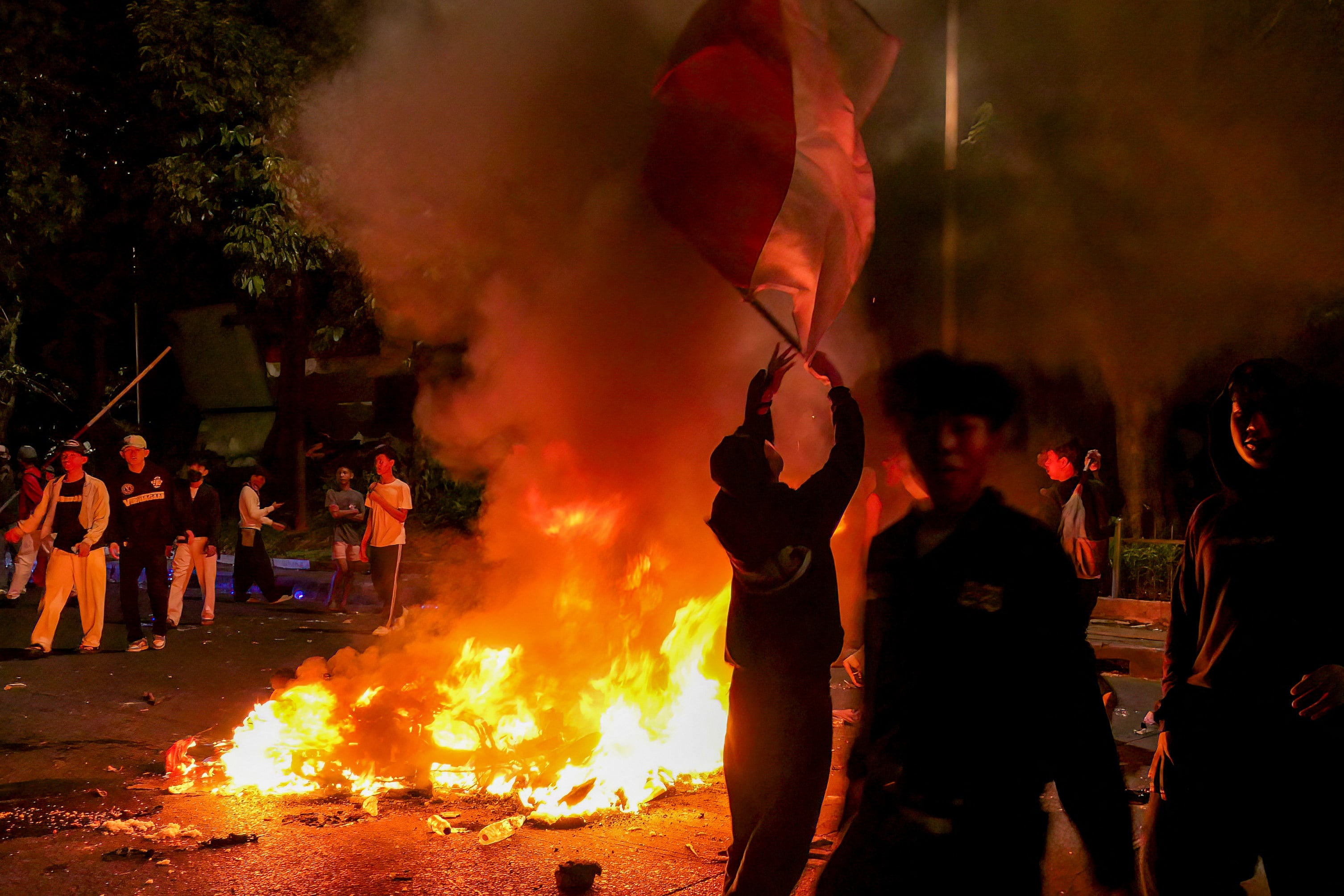 Protesters walk past a burning police motorcycle as a man waves a flag of Indonesia during a demonstration urging lawmakers to immediately pass an asset forfeiture law for corrupt officials outside the Parliament building in Jakarta on August 27, 2026. (Photo by AZWAR IPANK / AFP)