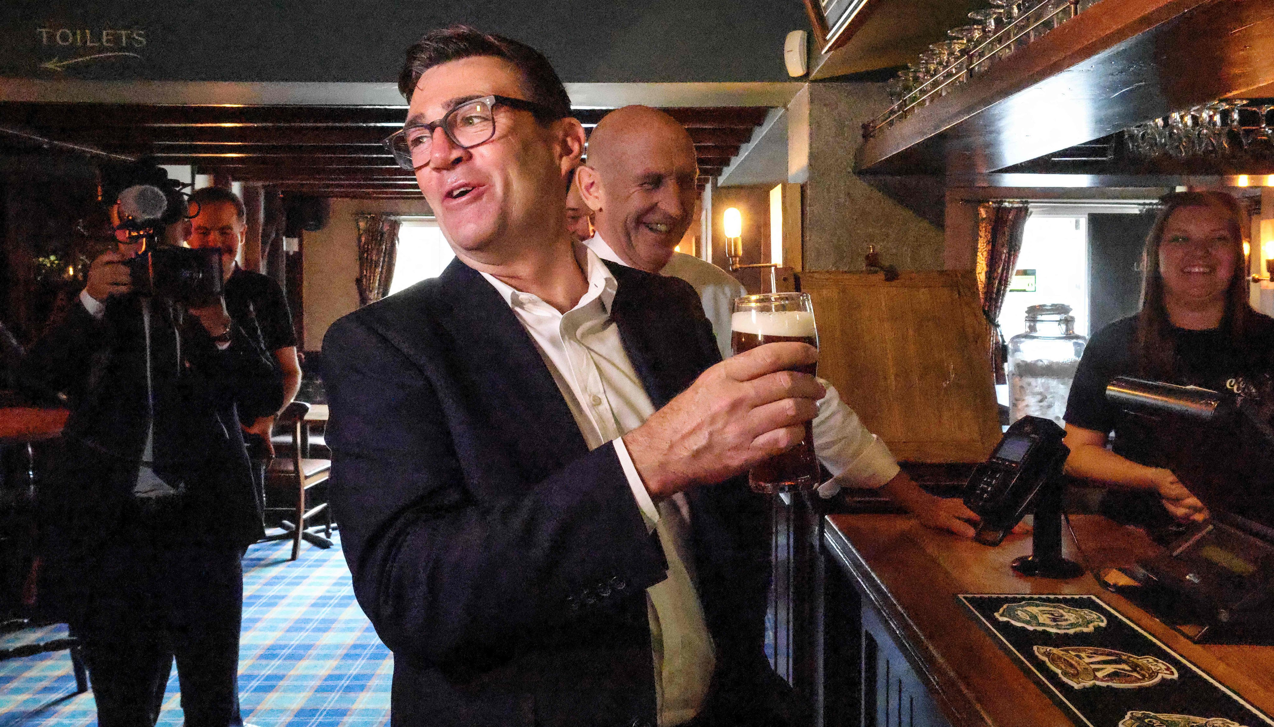 Britain’s Prime Minister Andy Burnham holds a pint of beer during a visit to the Hare Inn in Harlow, east of London with the Chancellor John Healy (centre) on July 23. Photo: AFP