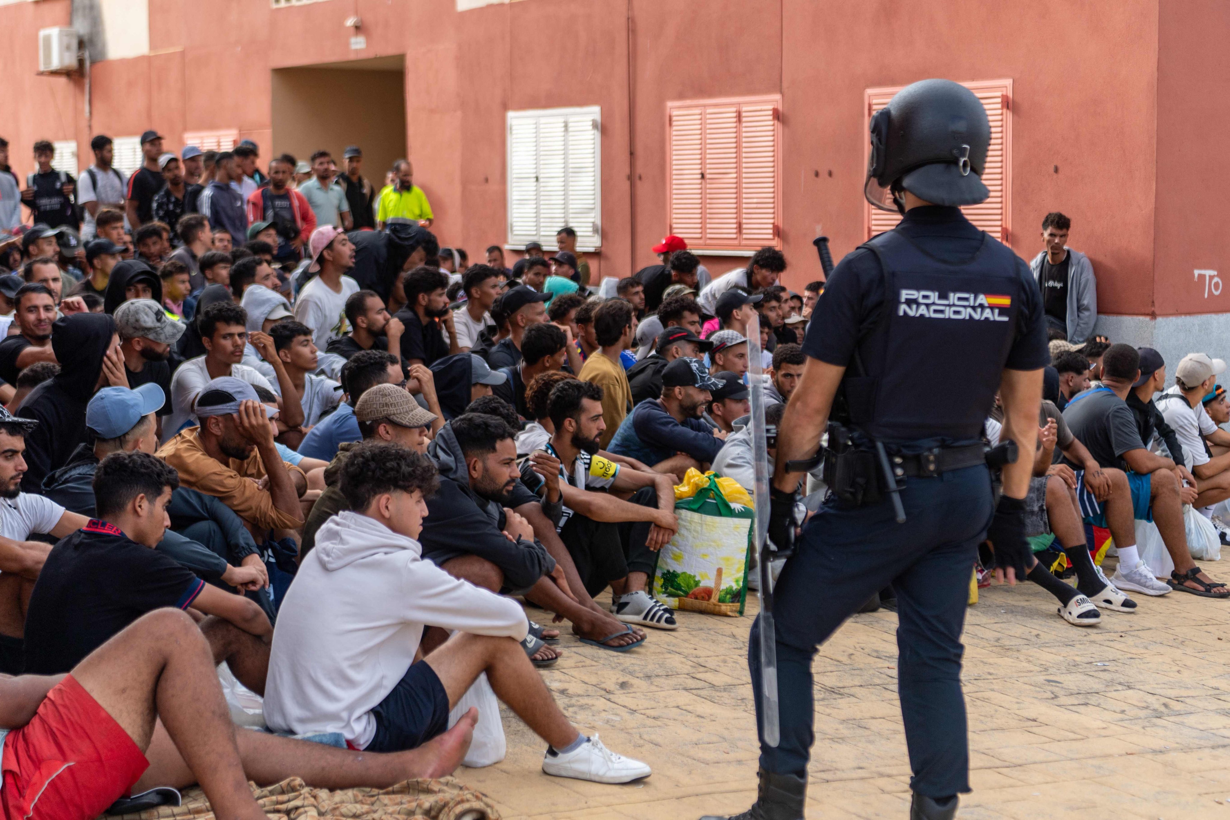 Spain’s National Police officers stand as migrants wait before being registered in a district of Ceuta on Monday. Photo: AFP