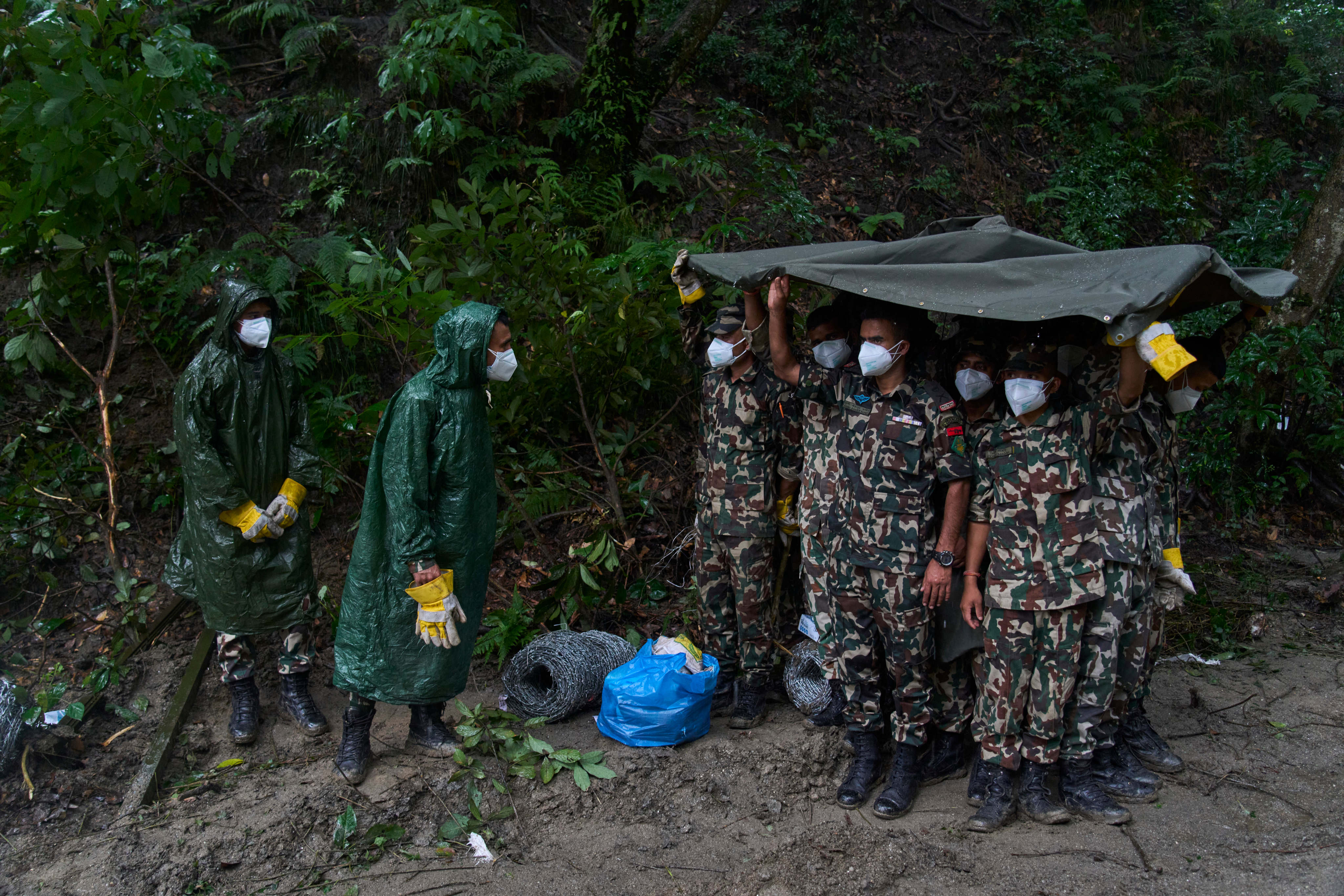 Nepalese army personnel take cover from the rain as they prepare the ground for the mass burial of flash flood victims in Kathmandu, Nepal, on Tuesday. Photo: AP