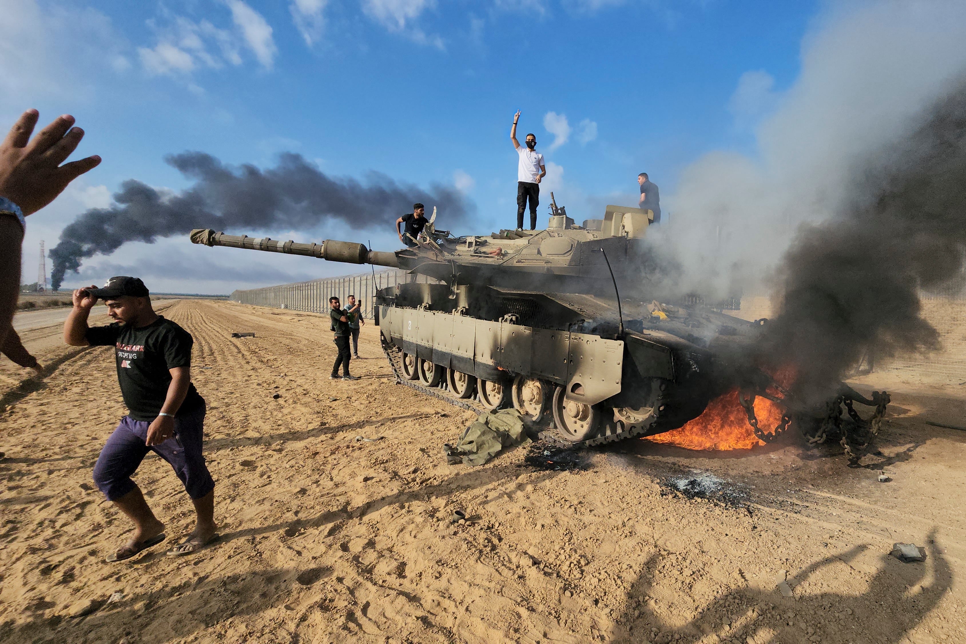 Palestinians celebrate by a destroyed Israeli tank at the Gaza Strip fence on October 7, 2023. Photo: AP