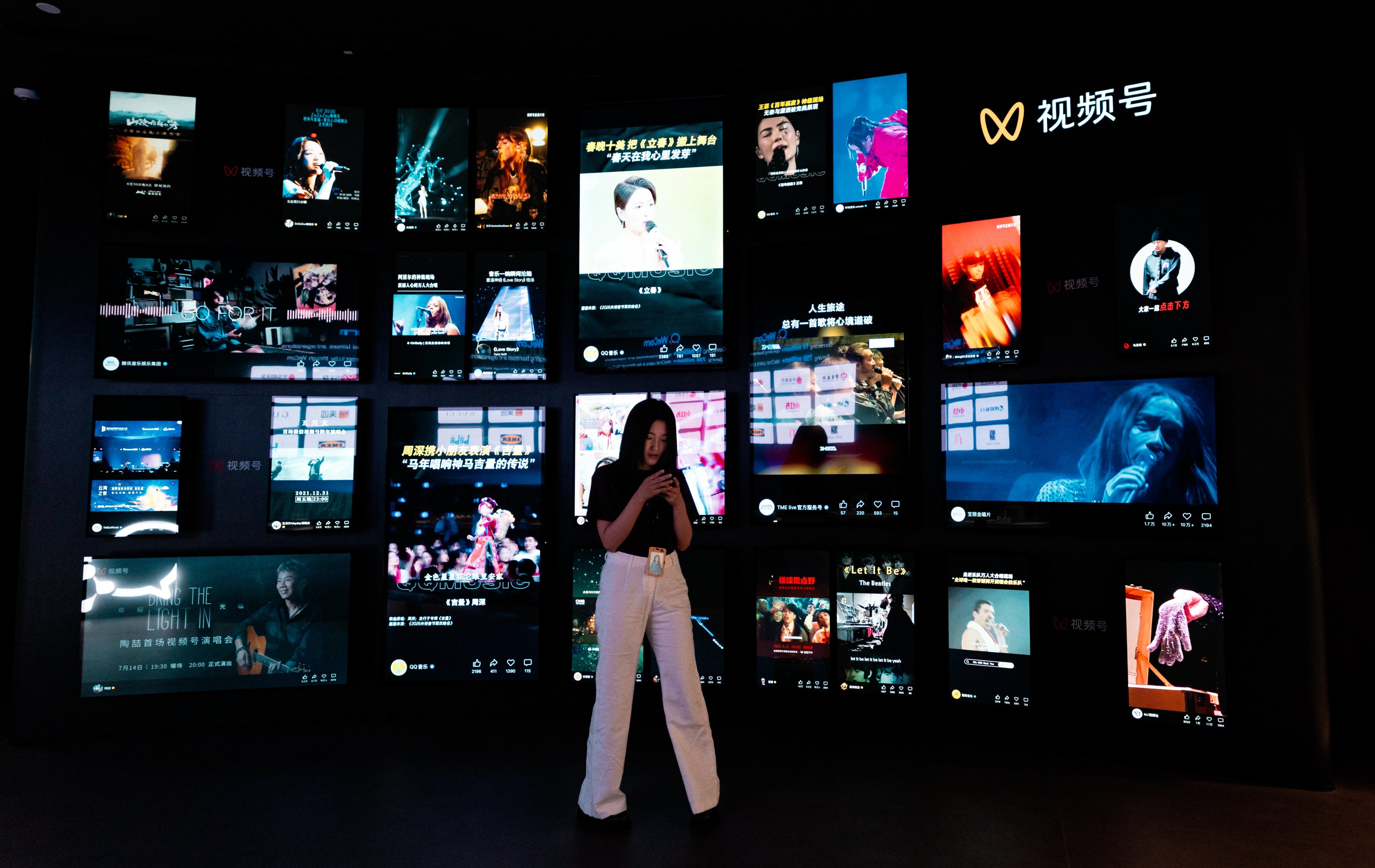 A woman uses her phone in front of a video wall in Tencent headquarters in Shenzhen on April 17, 2026. Photo: EPA