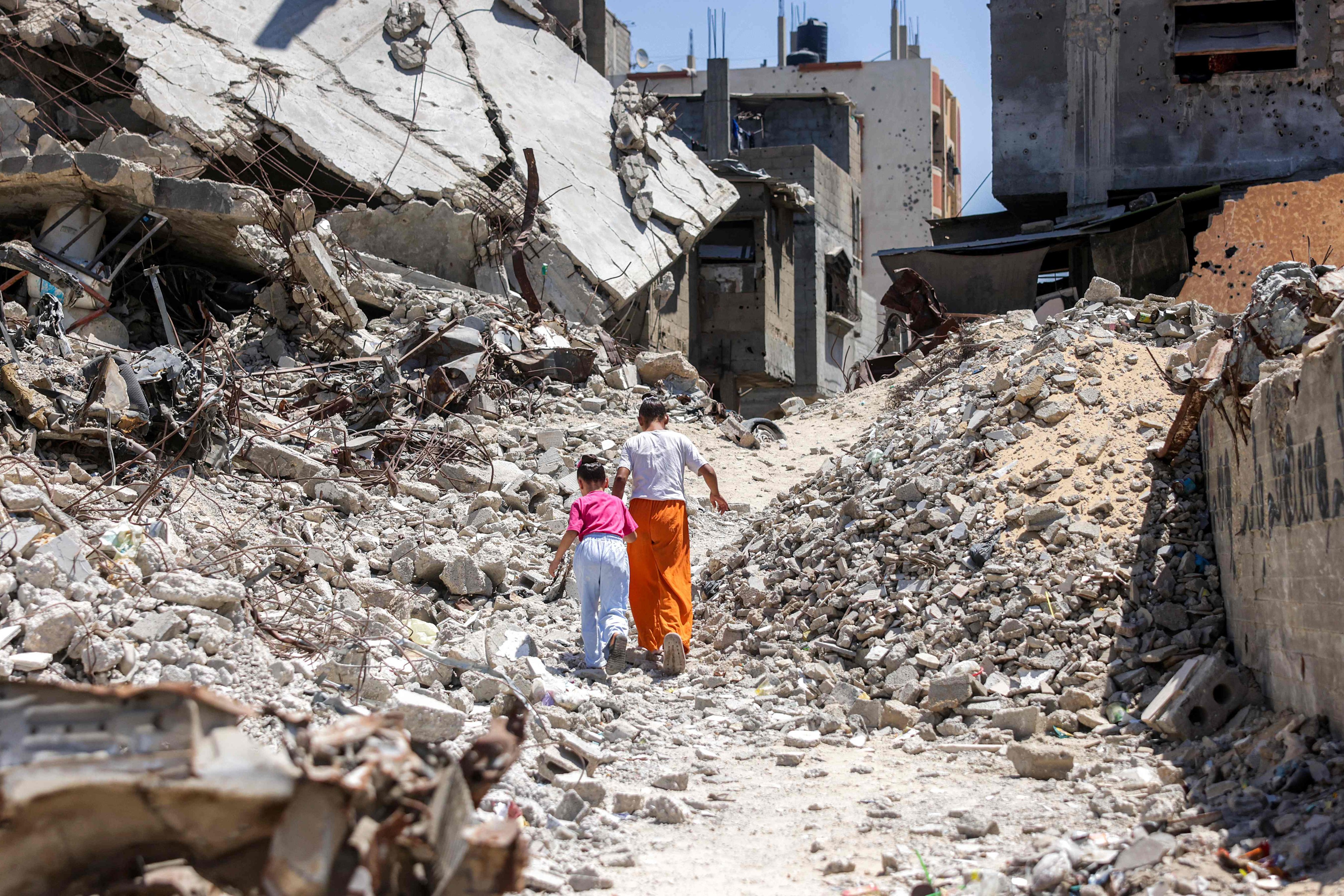 Two girls walk past the rubble of collapsed buildings in Khan Younis in the southern Gaza Strip on August 25. Photo: AFP
