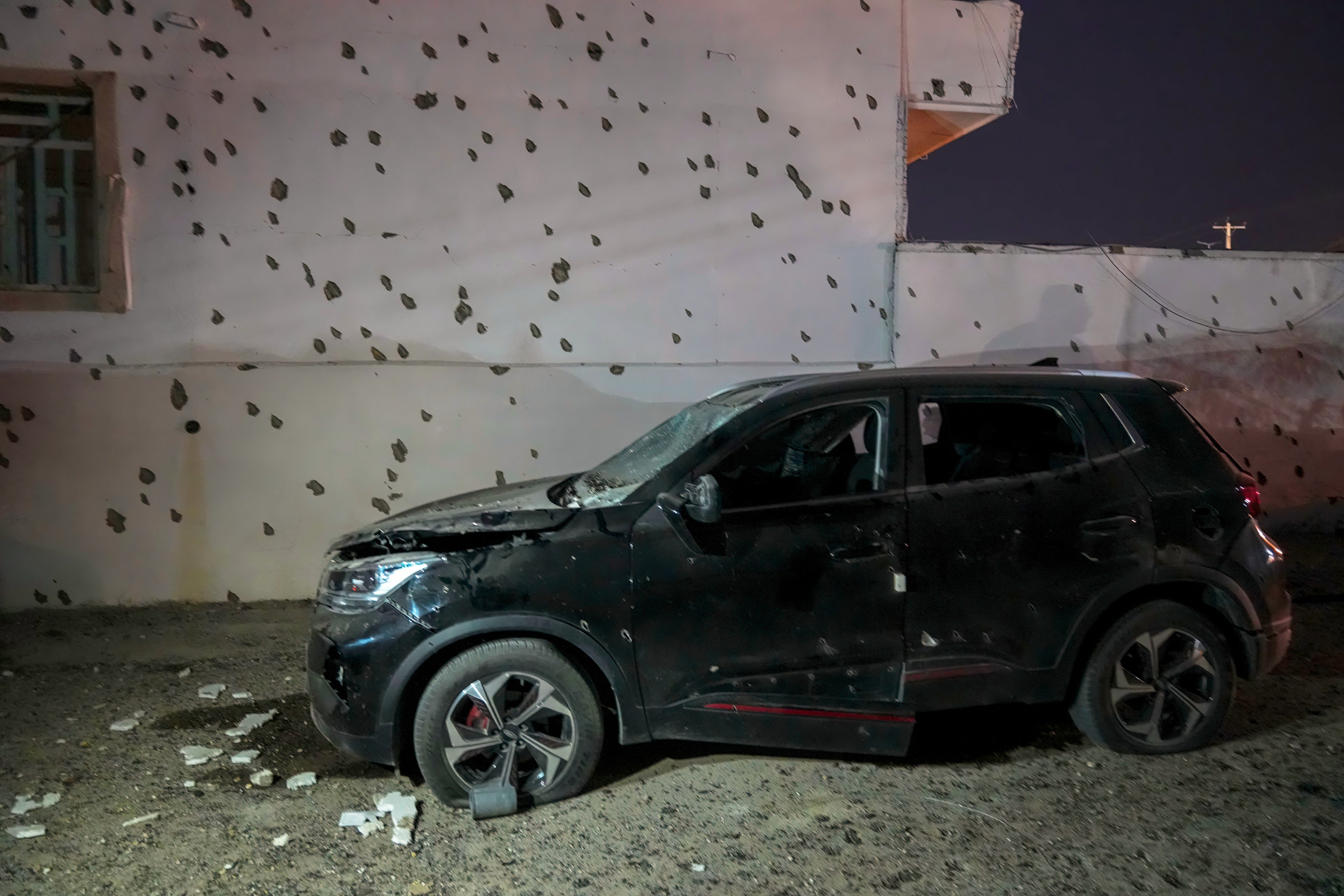 A damaged car beside a wall bearing numerous impact marks near the site of a strike in Lamerd, southern Iran, on February 28. Photo: Tasnim News Agency via AP