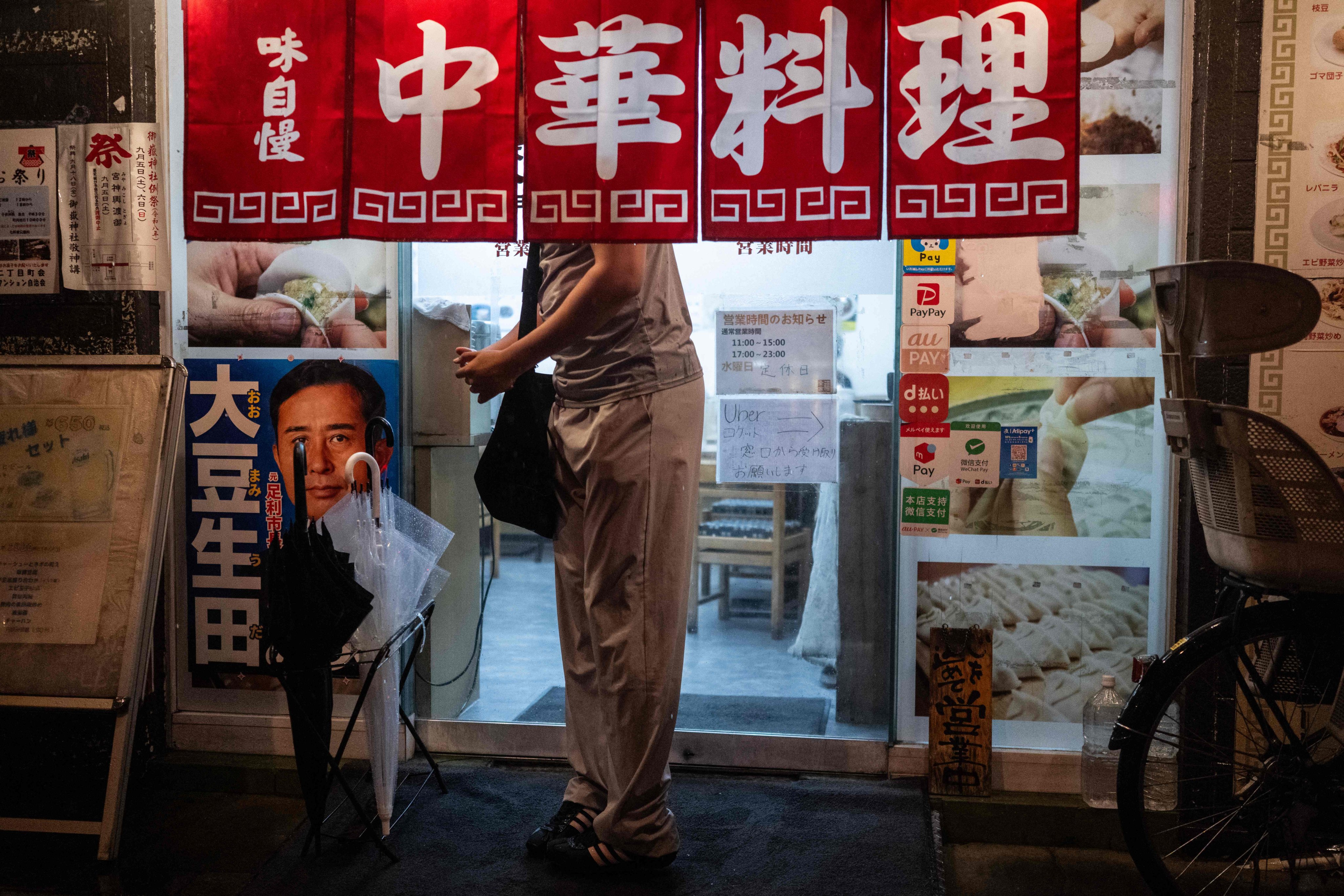 A man takes shelter under the awning of a restaurant as he waits to cross the street during a heavy rainstorm in Tokyo on Sunday. Photo: AFP