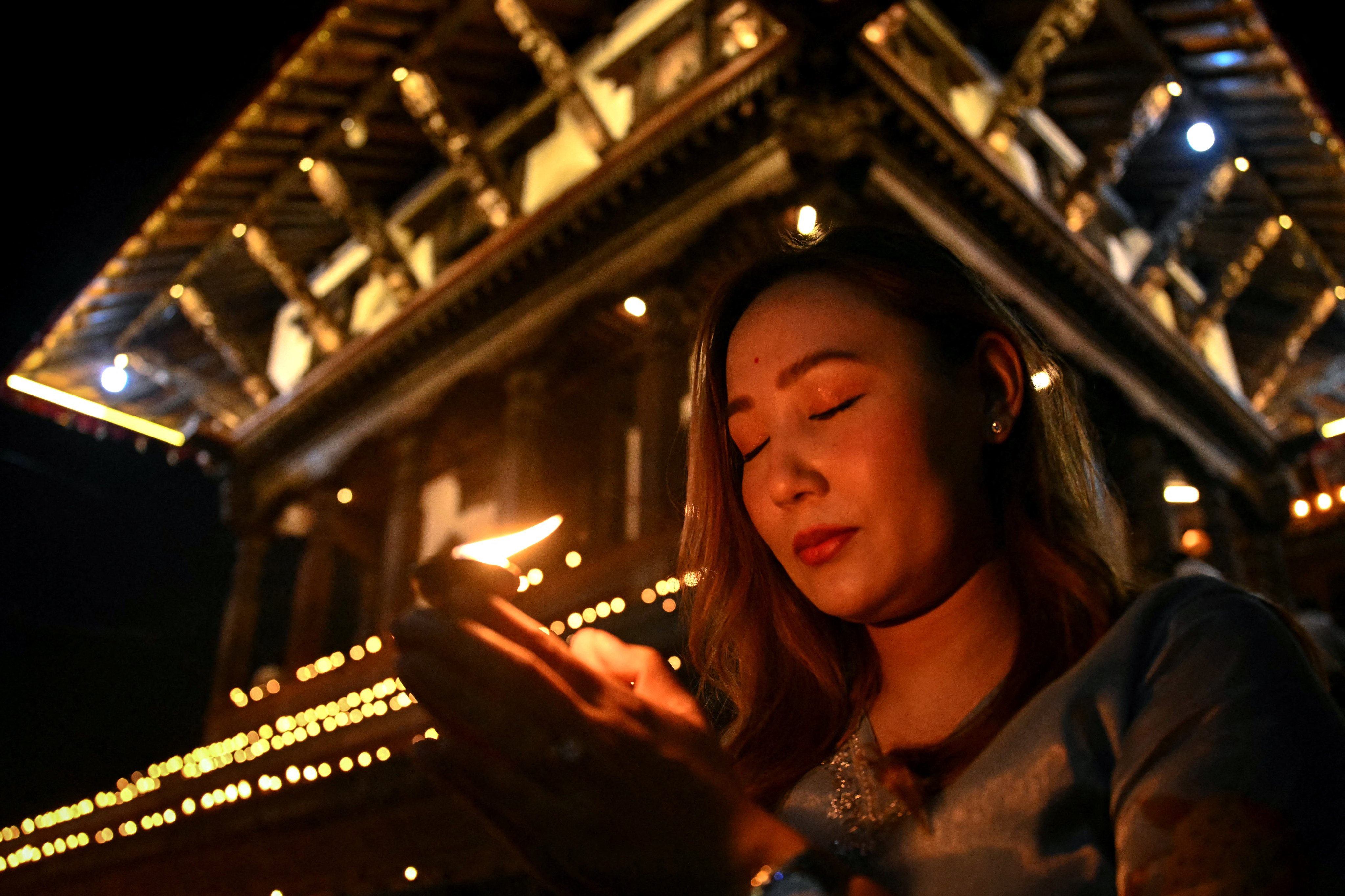 A woman holds an earthen lamp during a gathering at Durbar Square to observe a national day of mourning for victims of flash floods in Kathmandu on September 7, 2026. Nepal held a national day of mourning on September 7 for victims of devastating glacial floods, as families of missing hydropower workers feared trapped in tunnels prayed rescuers might yet find them alive. (Photo by Prakash MATHEMA / AFP)