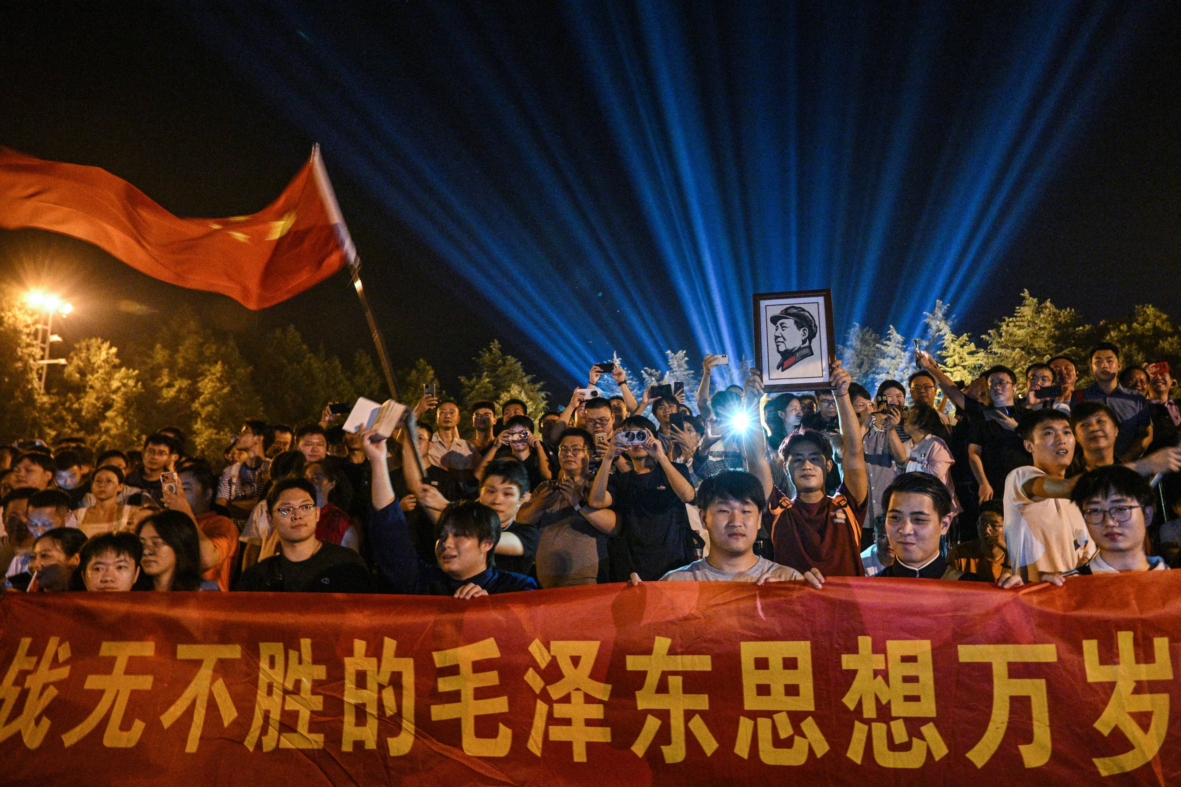 A man holds a portrait of late Communist leader Mao Zedong as people gather to pay tribute at the Bronze Statue Square in Shaoshan, China’s central Hunan province on September 8, 2026, a day before the 50th anniversary of his death. (Photo by Hector RETAMAL / AFP)