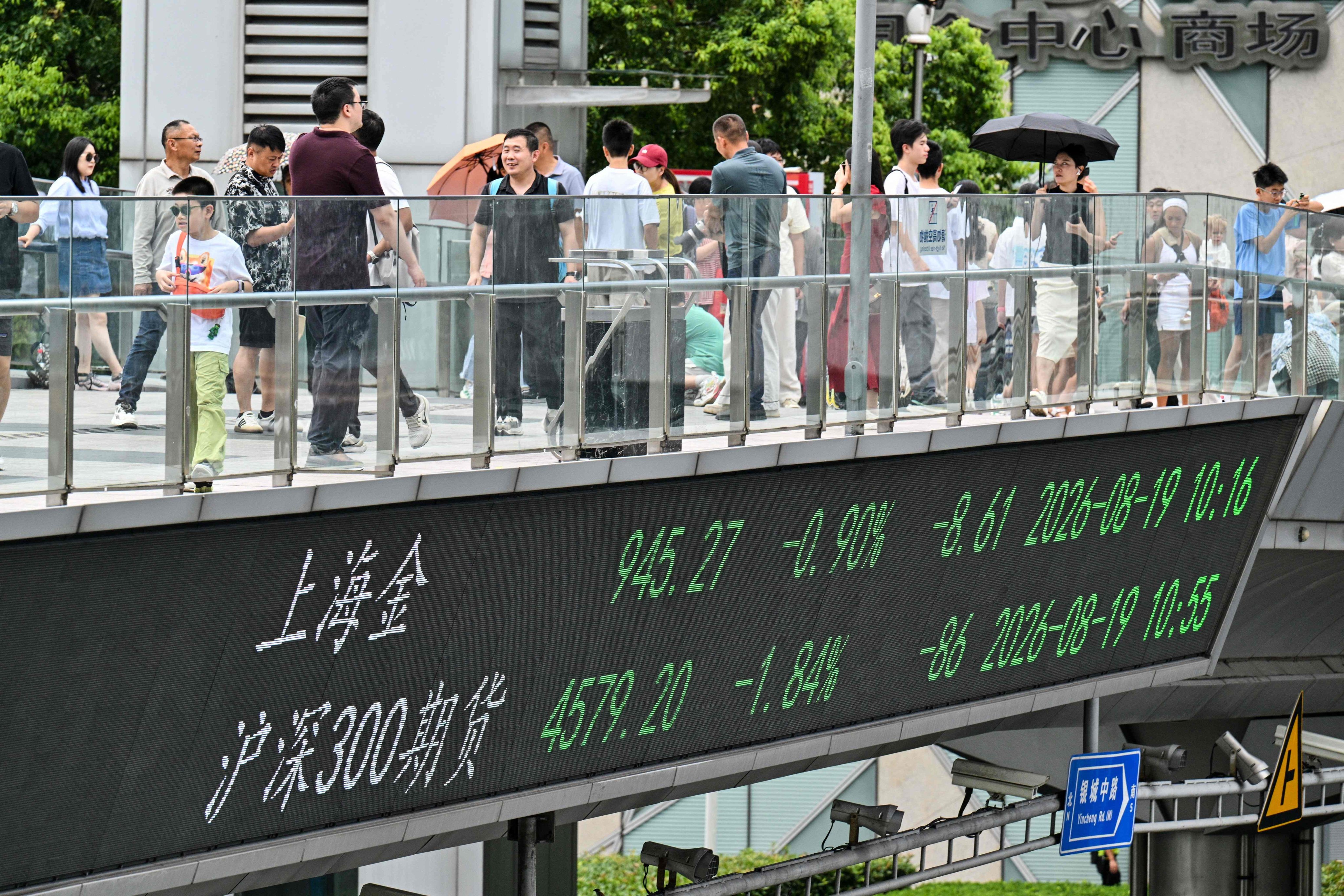 People walk across a footbridge with a screen showing financial market movements, in the financial district of Shanghai on August 19. Photo: AFP