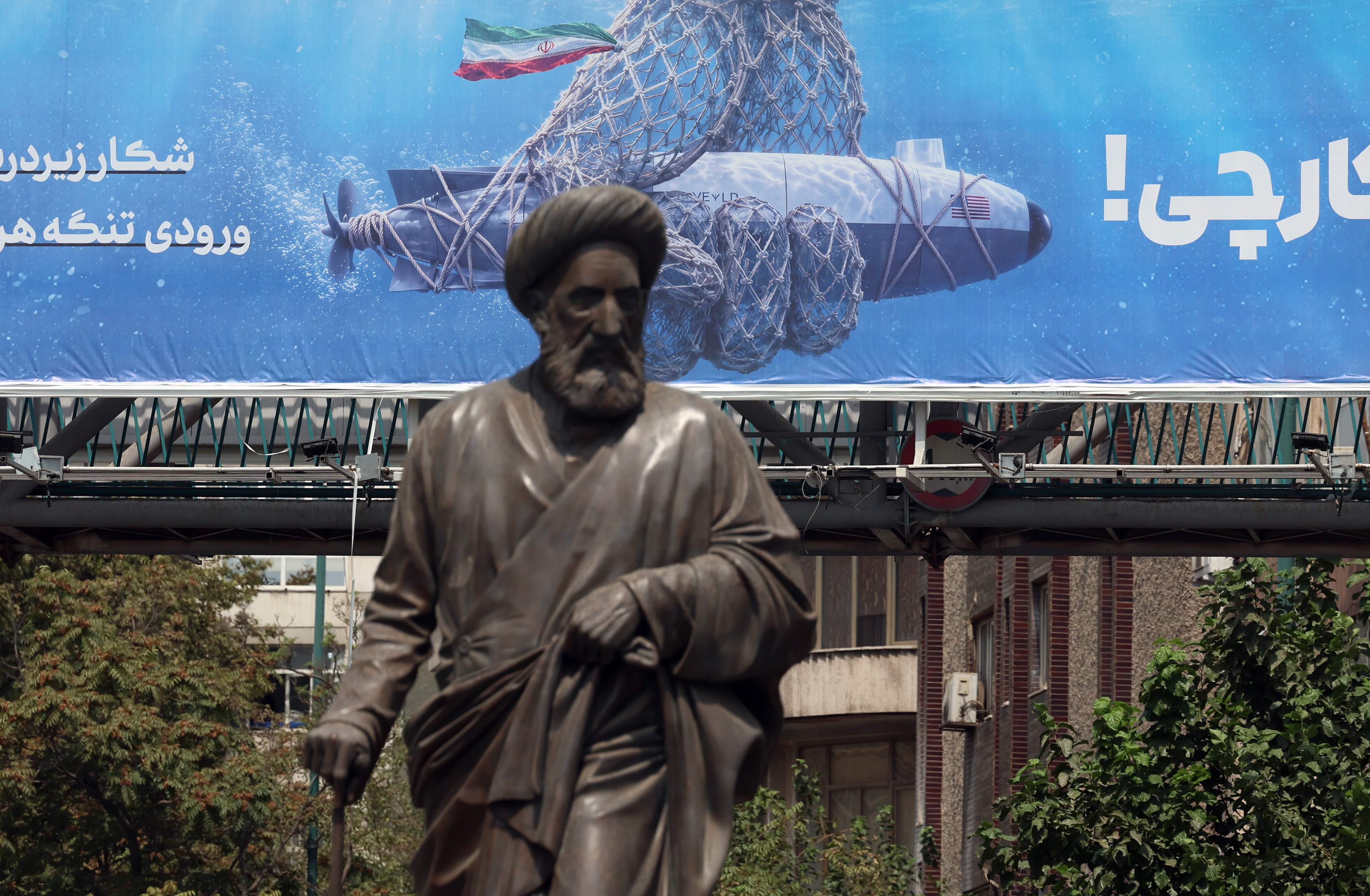 A statue stands in front of a billboard featuring a captured US underwater drone with text reading in Persian, ‘Hunting the Hunter’, in Tehran, Iran, on Wednesday. Photo: EPA