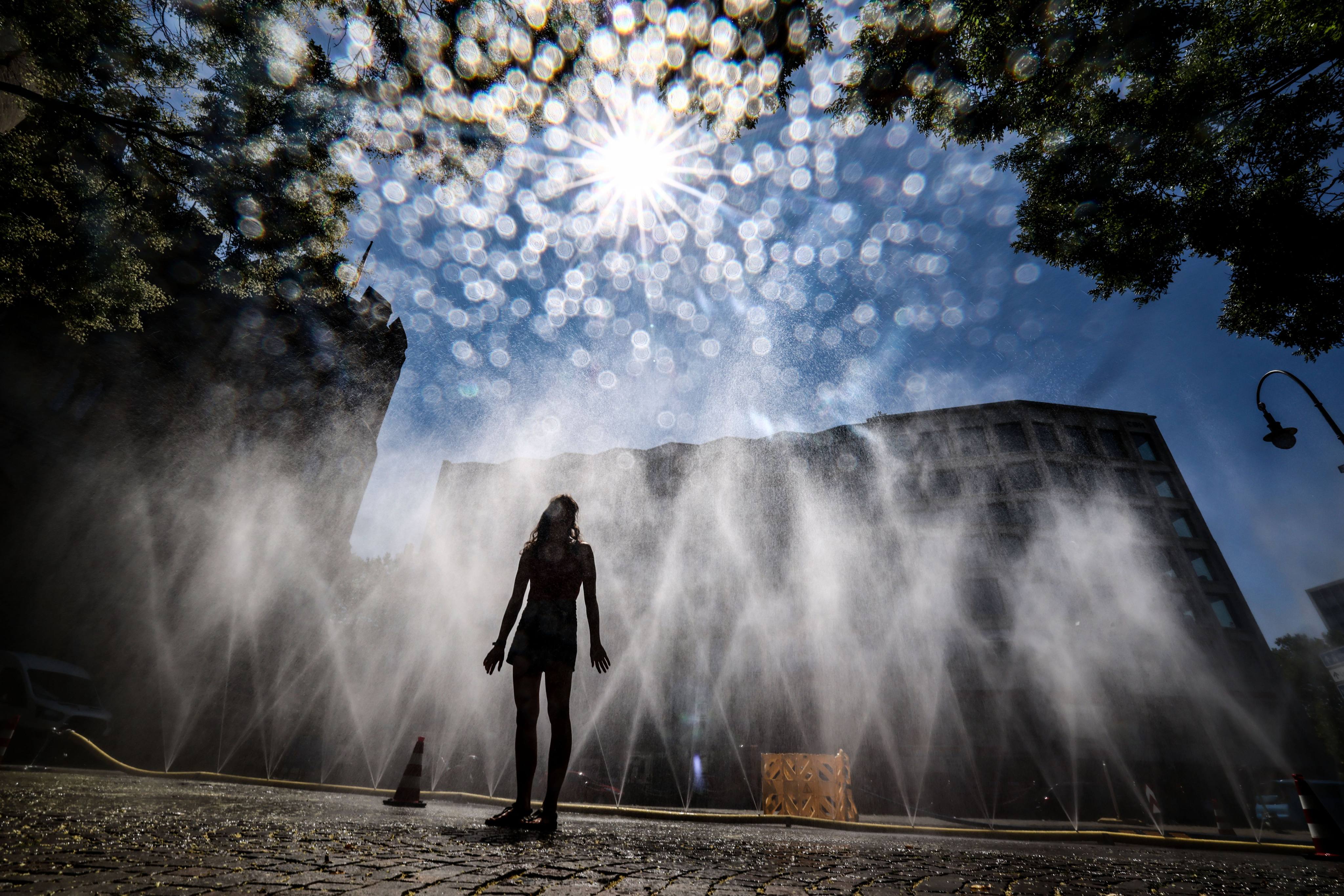 A woman stands in front of a hose spraying a mist of water in Cologne, Germany. Photo: dpa
