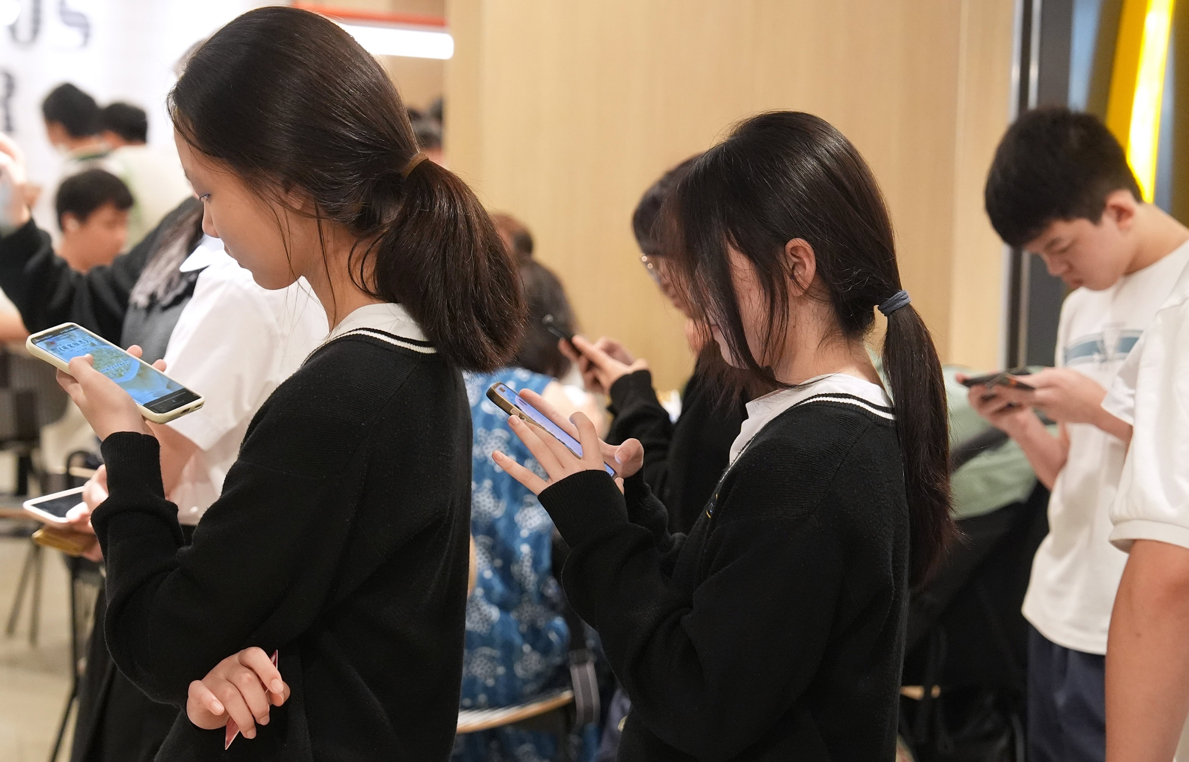 Students use their smartphones while queuing outside a restaurant in Tseung Kwan O on October 16,2025. Photo:  Elson Li
