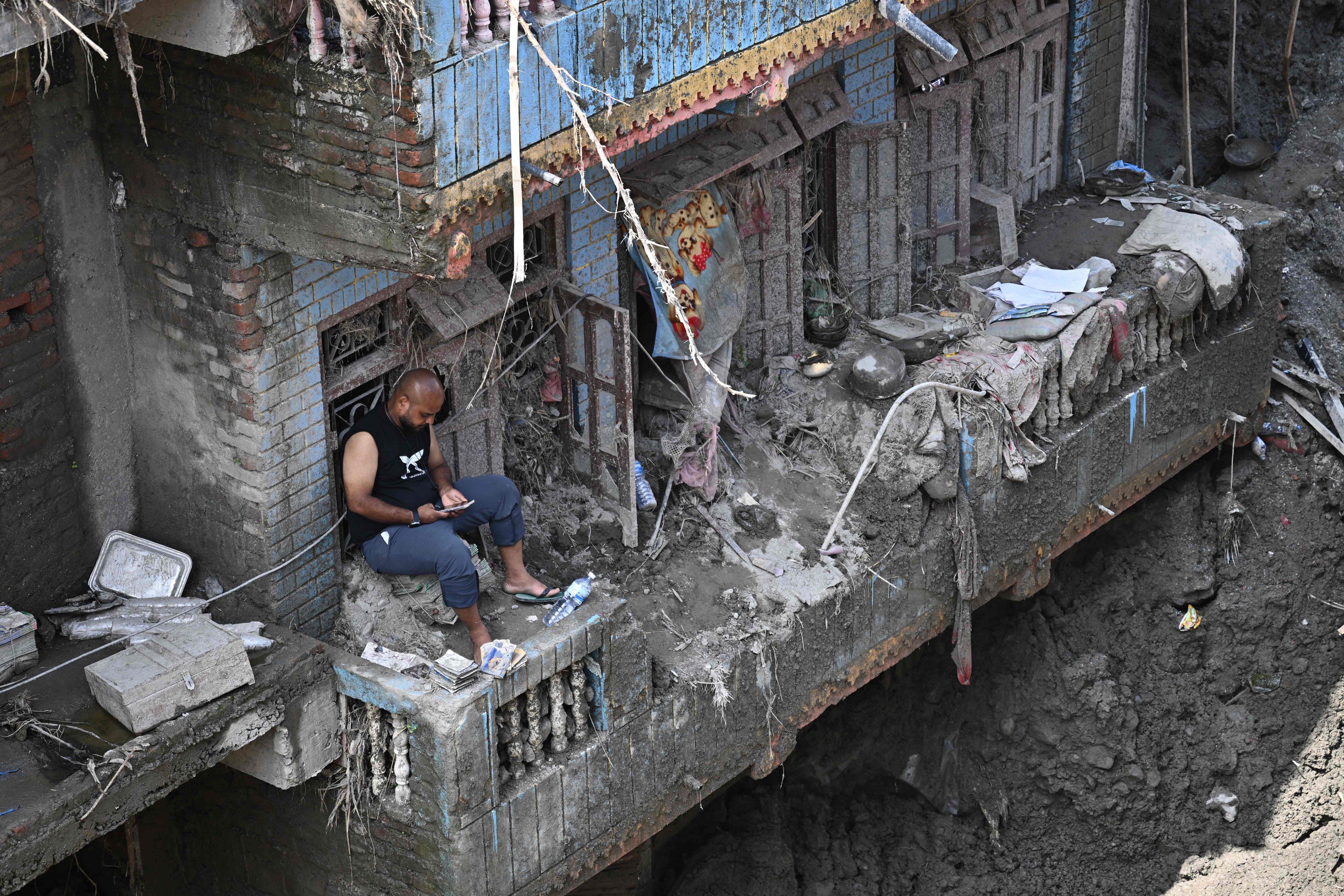A man sits on the balcony of a sludge-ridden house in Nepal’s Nuwakot district on September 8. The August 26 glacial and mountain collapse on the China-Nepal border killed at least 1,398 people, with more than 5,500 missing, including around 800 foreigners. Photo: AFP