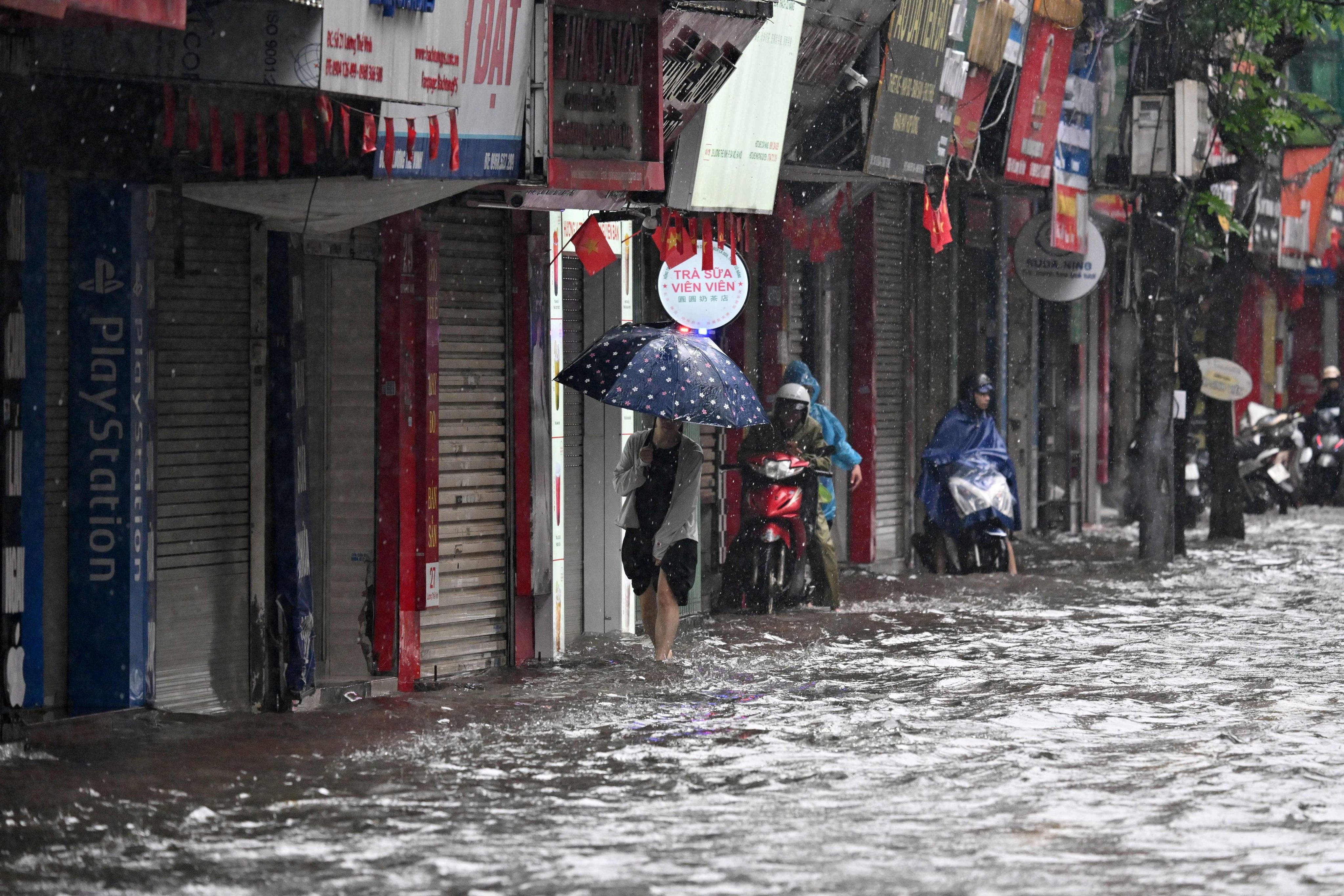 A woman wades along a flooded sidewalk in Hanoi on Thursday. Photo: AFP