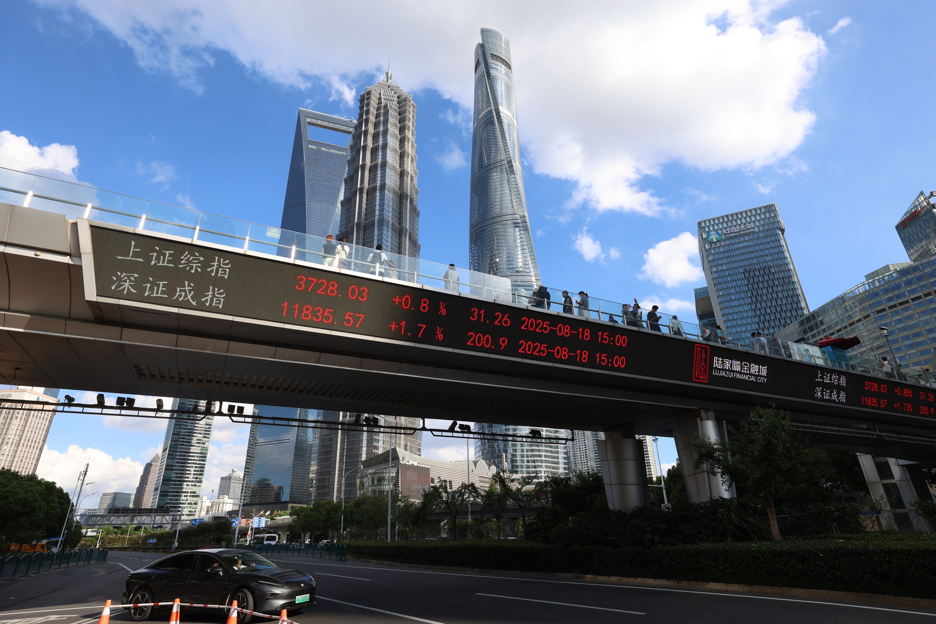 Buildings in Shanghai tower over a pedestrian bridge where a sign displays stock index information on August 18, 2025. Photo: VCG/VCG via Getty Images