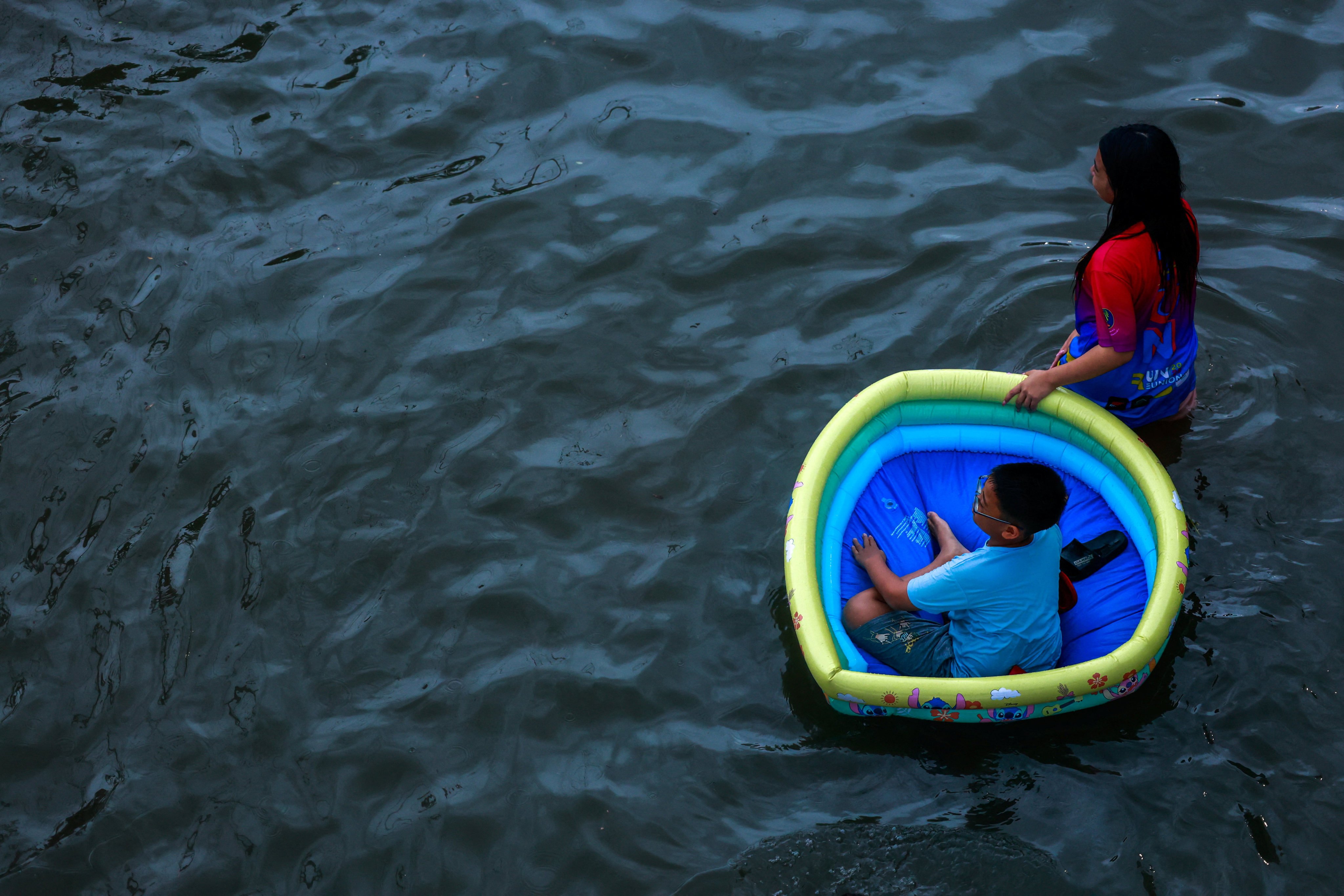 A woman pulls an inflatable swimming pool with a child in it as she wades through a flooded Bangkok street on Saturday. Photo: Reuters