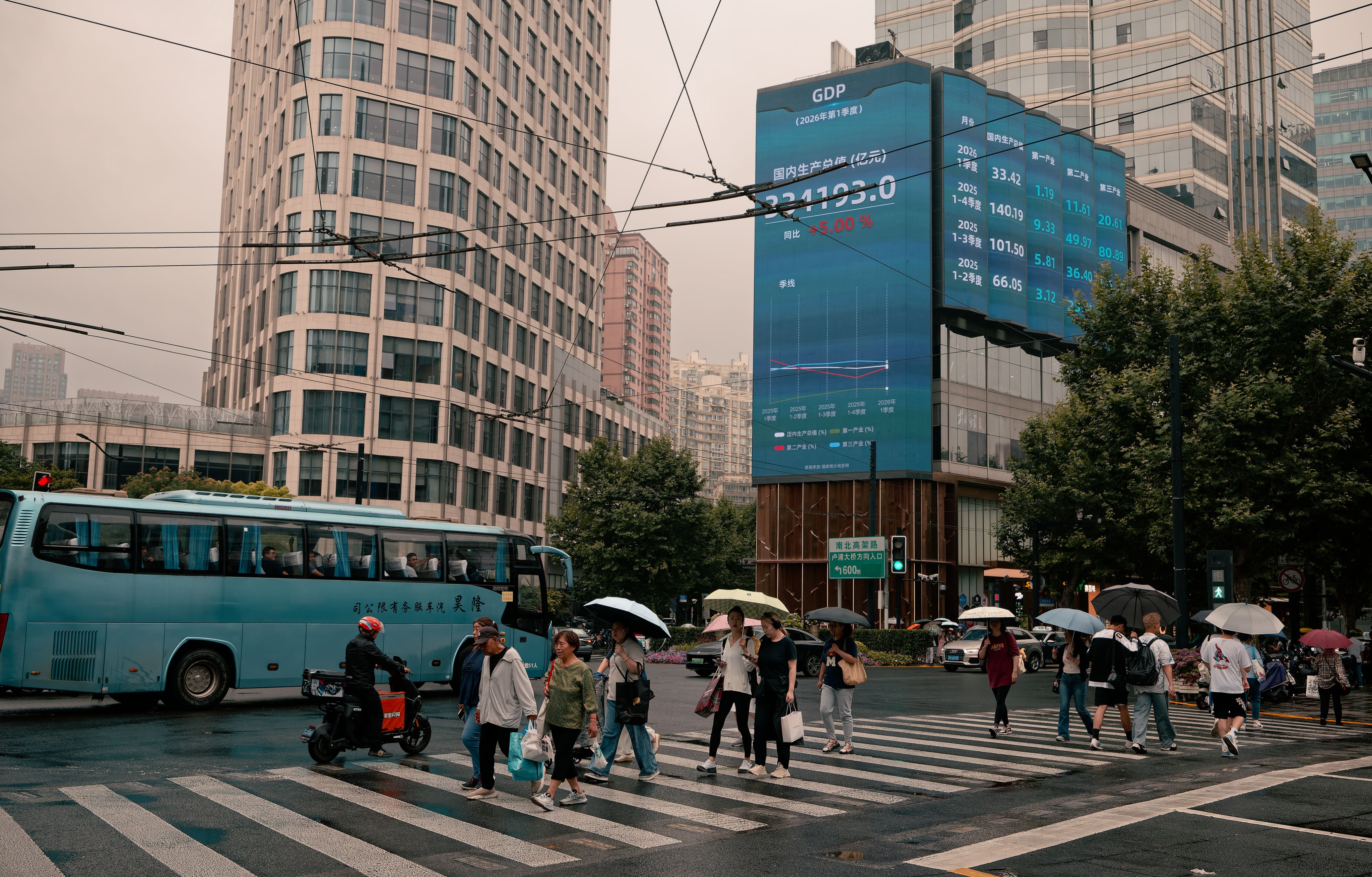 People walk on a street beneath a screen showing stock market and economic data in Shanghai, China. Photo: EPA