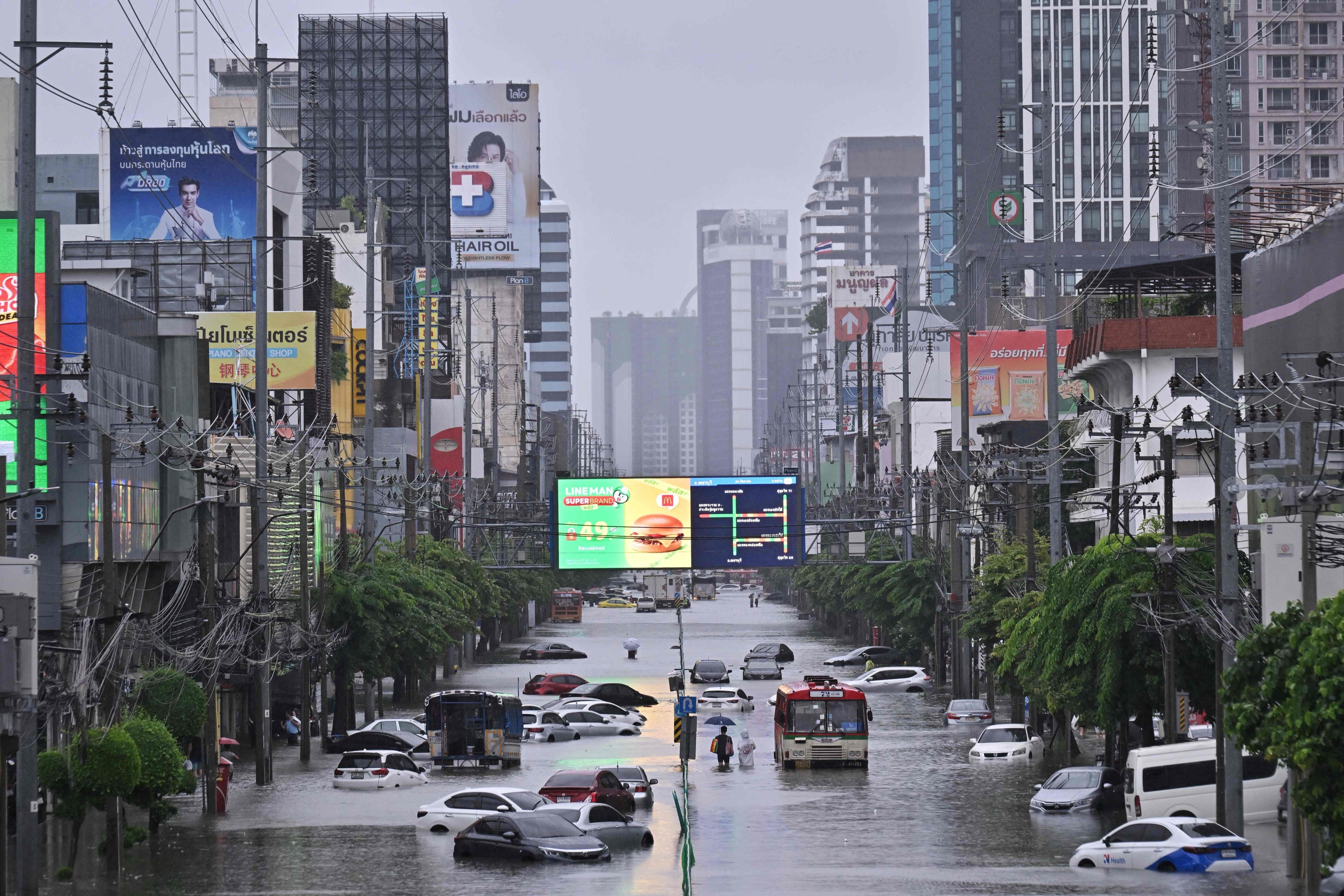 People walk past abandoned vehicles on a flooded Petchaburi Road in Bangkok on Saturday. Photo: AFP