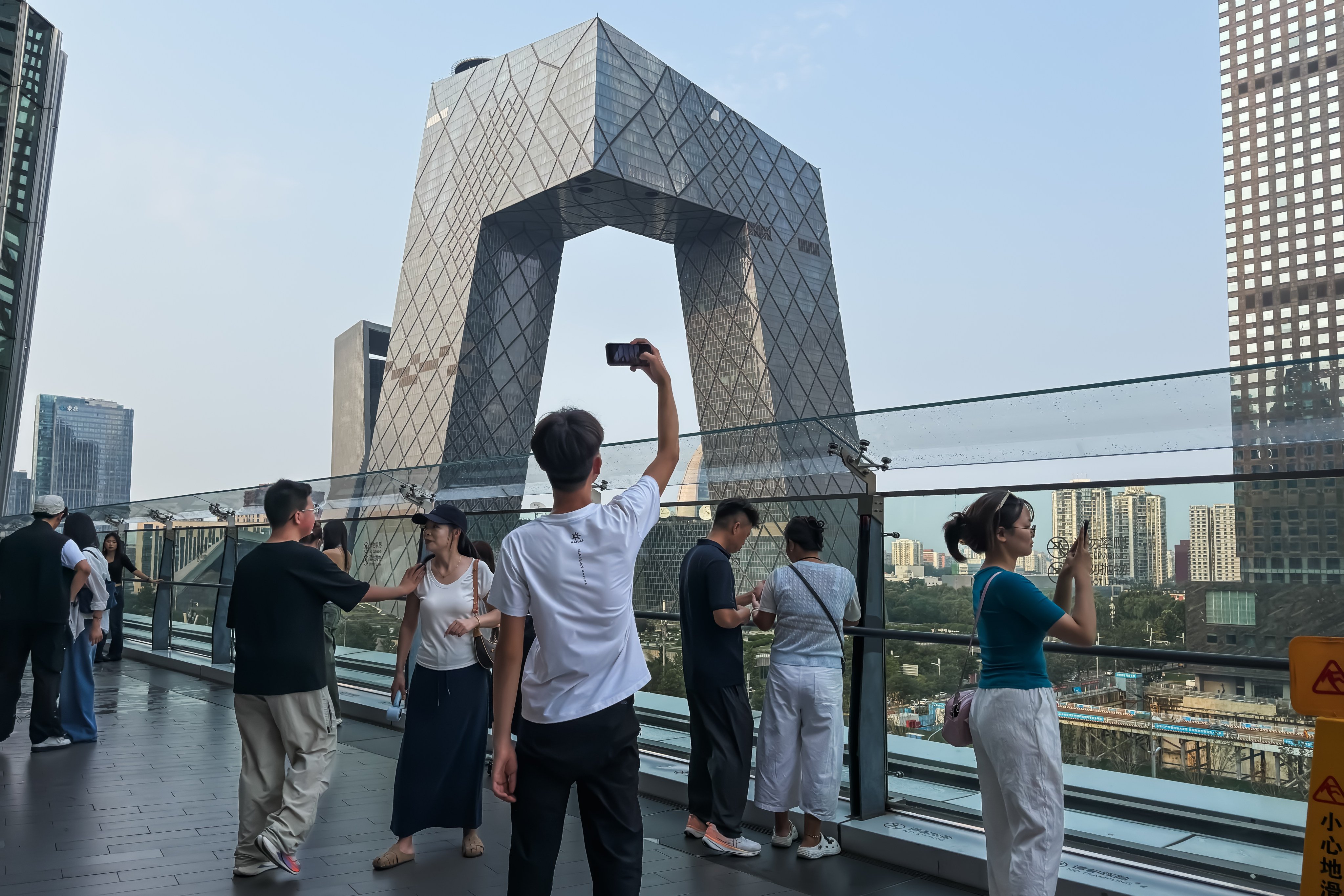 People take photographs from an elevated terrace overlooking the China Central Television headquarters on August 22. China is seeking to bolster domestic demand and sustain economic growth amid continued pressure from a prolonged property downturn, cautious consumer spending and global trade uncertainties. Photo: Getty Images
