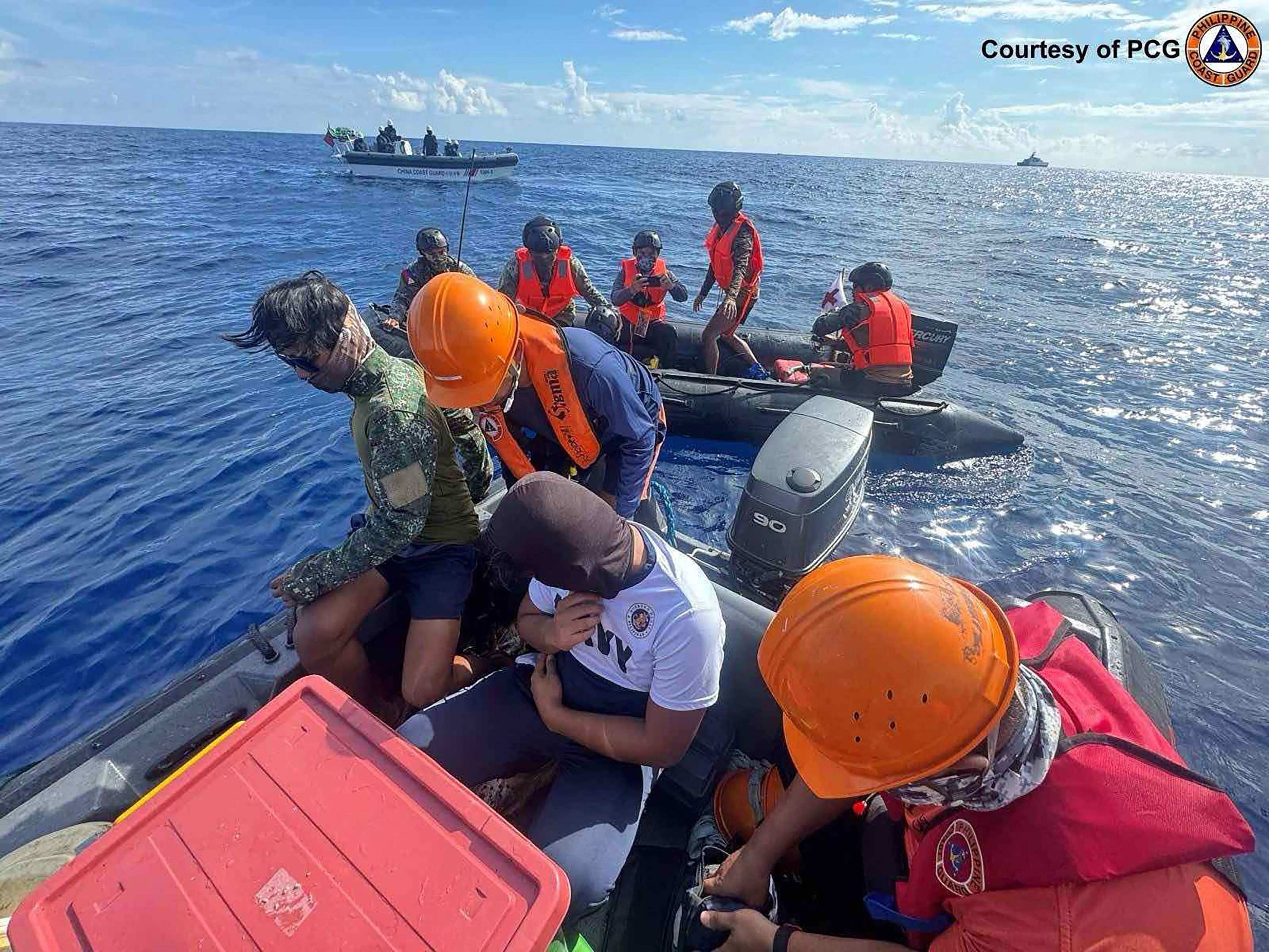 Philippine Navy personnel transfer a colleague to a Philippine Coast Guard rigid boat while Chinese Coast Guard personnel aboard their rigid boat watch on, during a medical evacuation near Second Thomas Shoal. Photo: Philippine Coast Guard/AFP