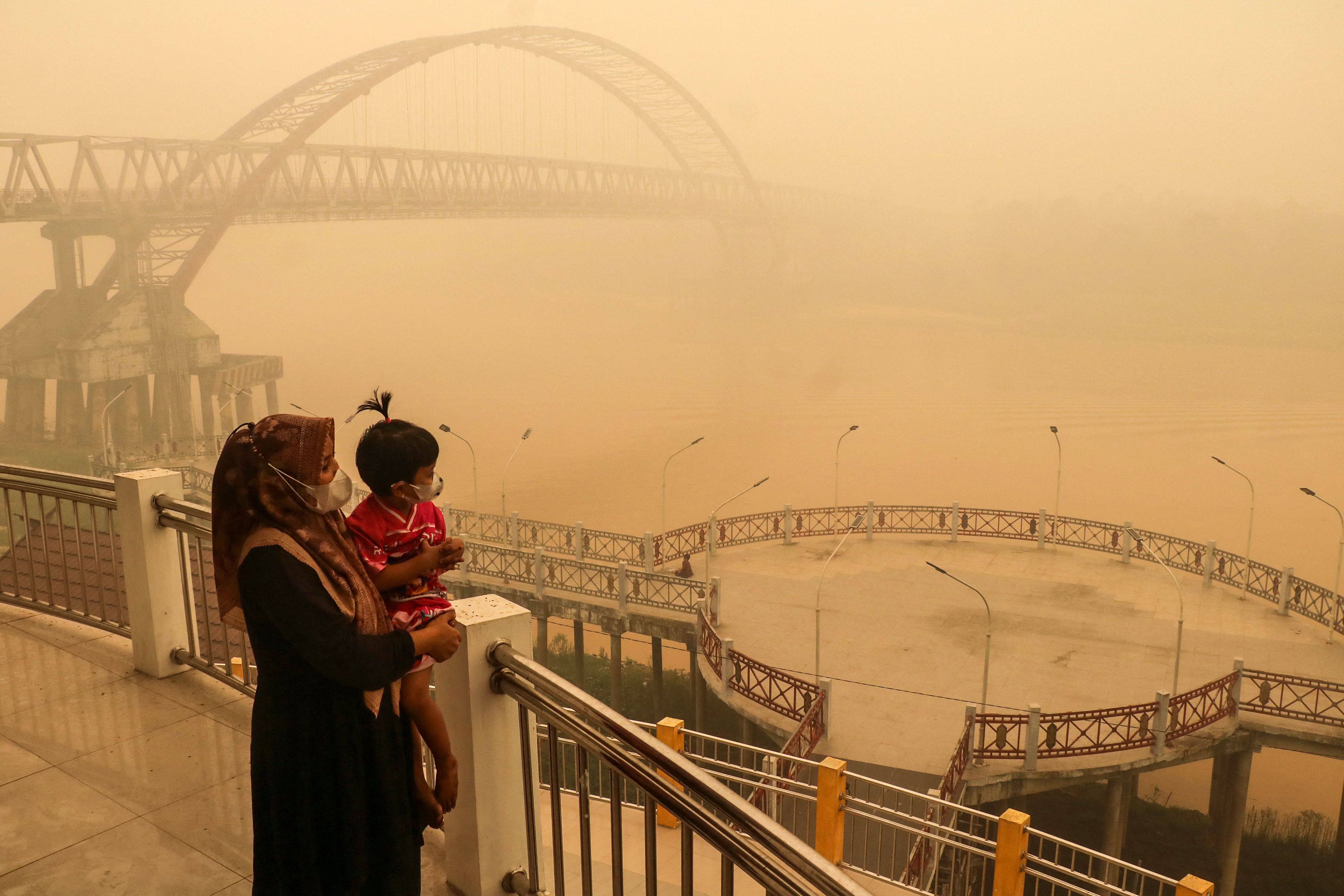 A child and mother wearing face masks look on from a bridge amid thick haze from forest and land fires in the region in Palangkaraya, Central Kalimantan, on Monday. Photo: AFP