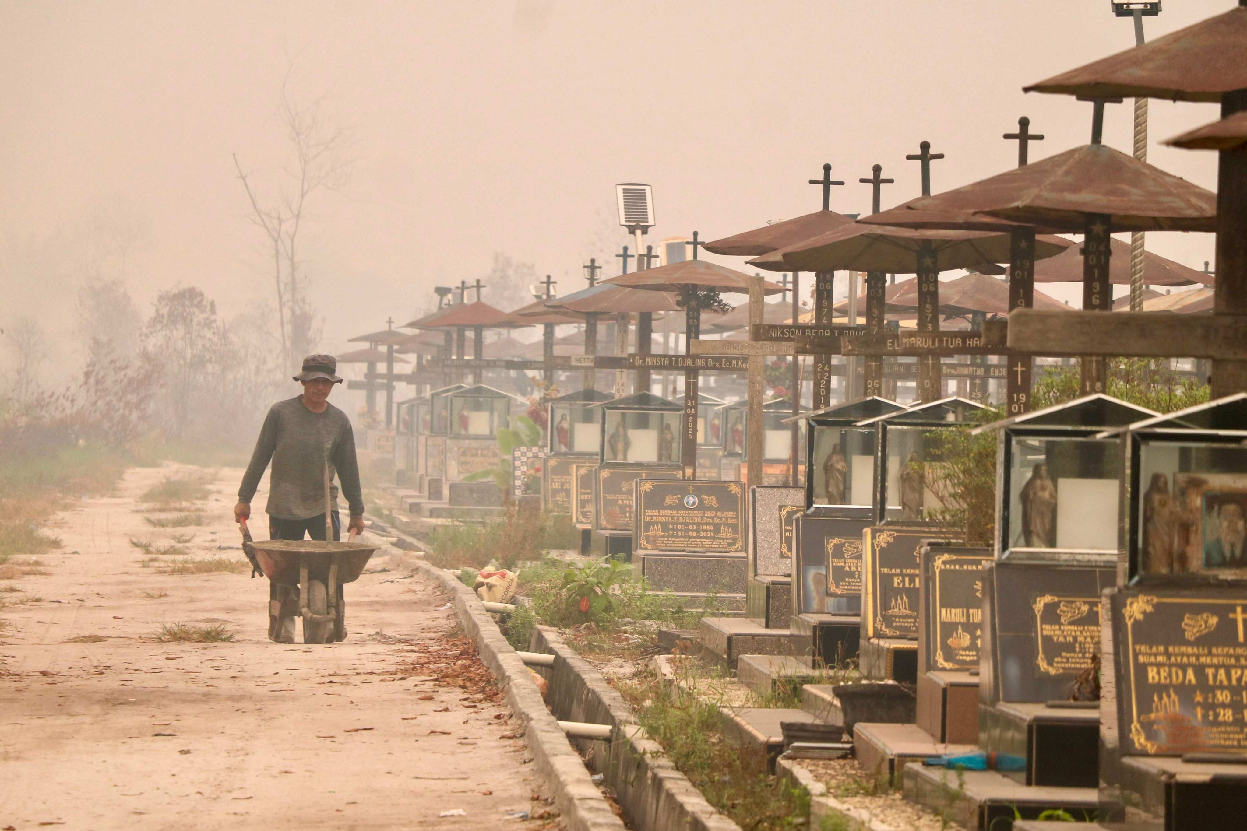 A worker pushes a wheelbarrow through a public cemetery blanketed in thick smoke haze caused by forest and land fires in Palangka Raya, Indonesia, on September 30, 2026. Photo: AFP