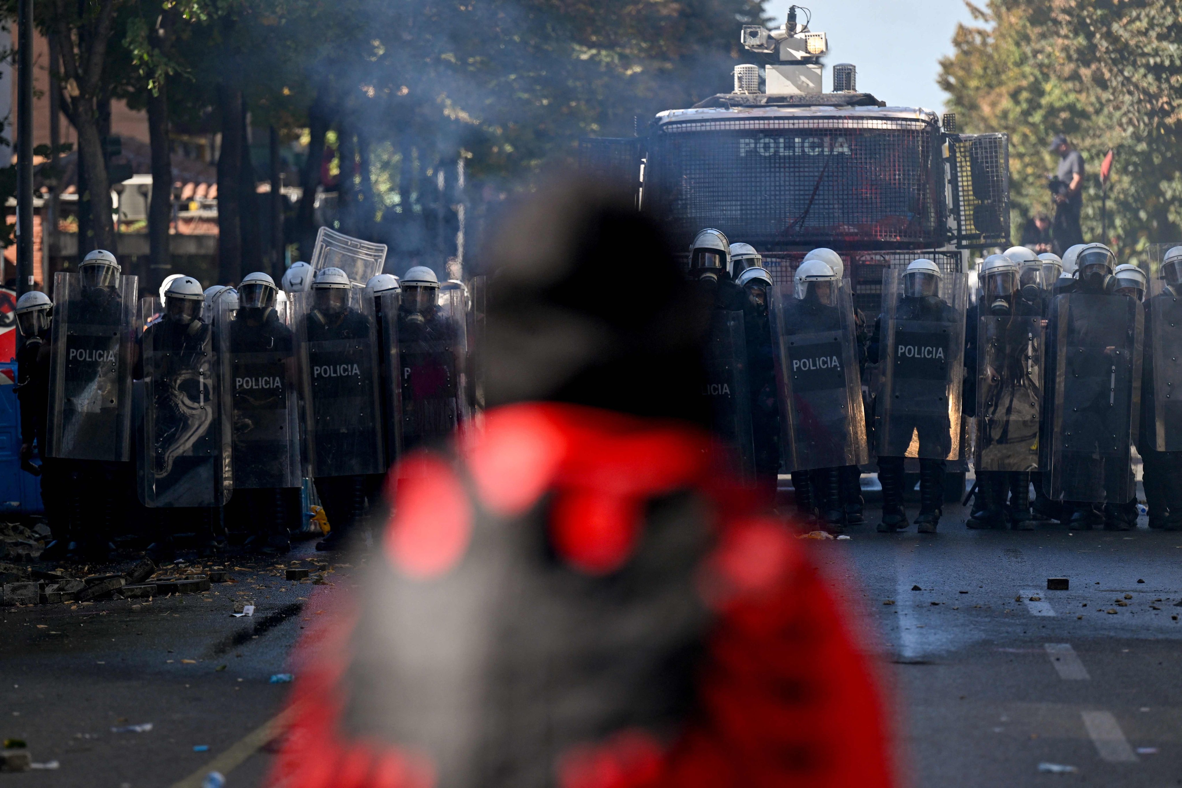 A protester wrapped in the Albanian flag faces off with riot police officers and a police water cannon vehicle in central Tirana on Saturday. Photo: AFP