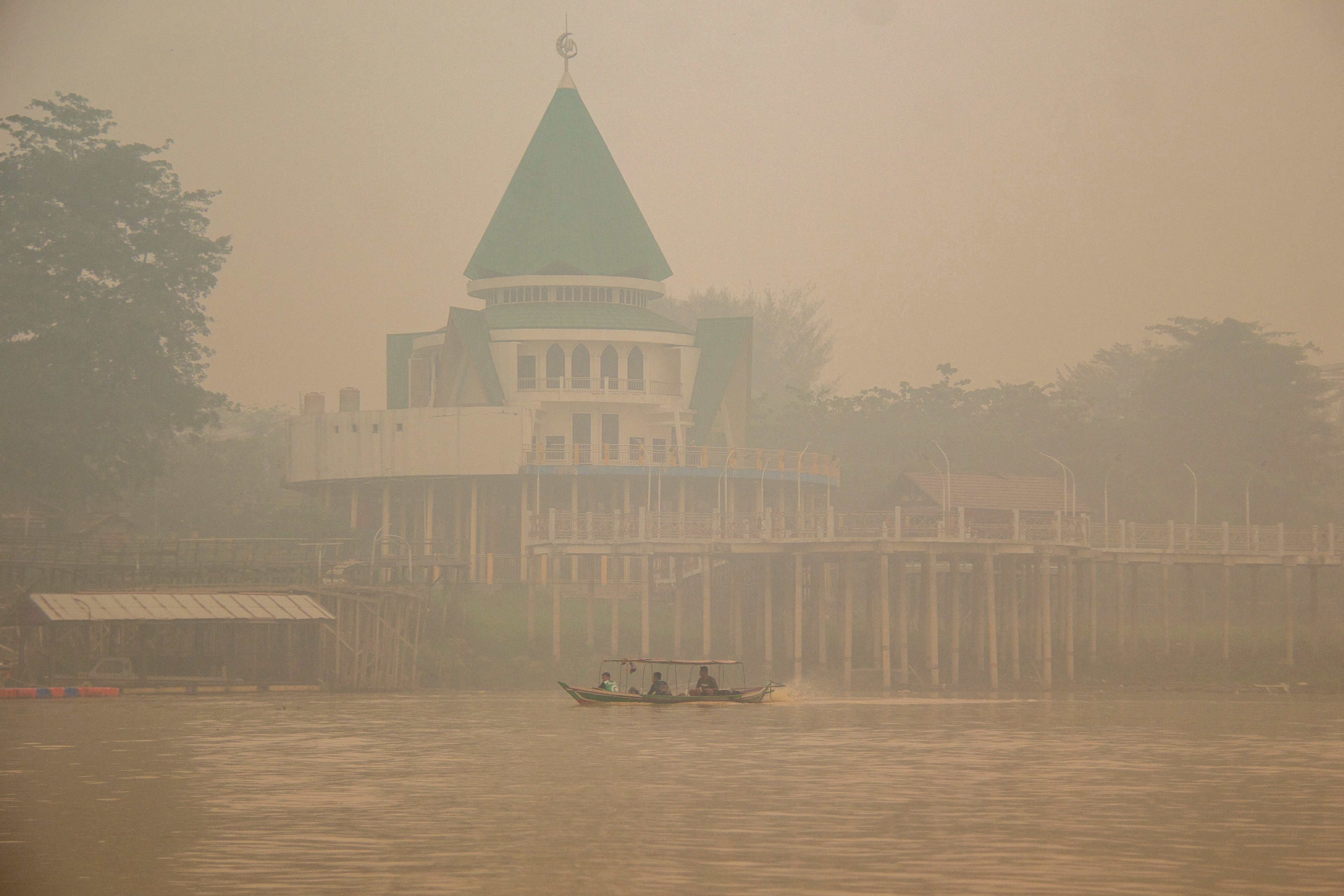 People ride a wooden boat on the Kahayan River as haze from wildfires shrouds Palangka Raya in Central Kalimantan province, Indonesia, October 18, 2026. REUTERS/Arief Rahman Septian Prathama