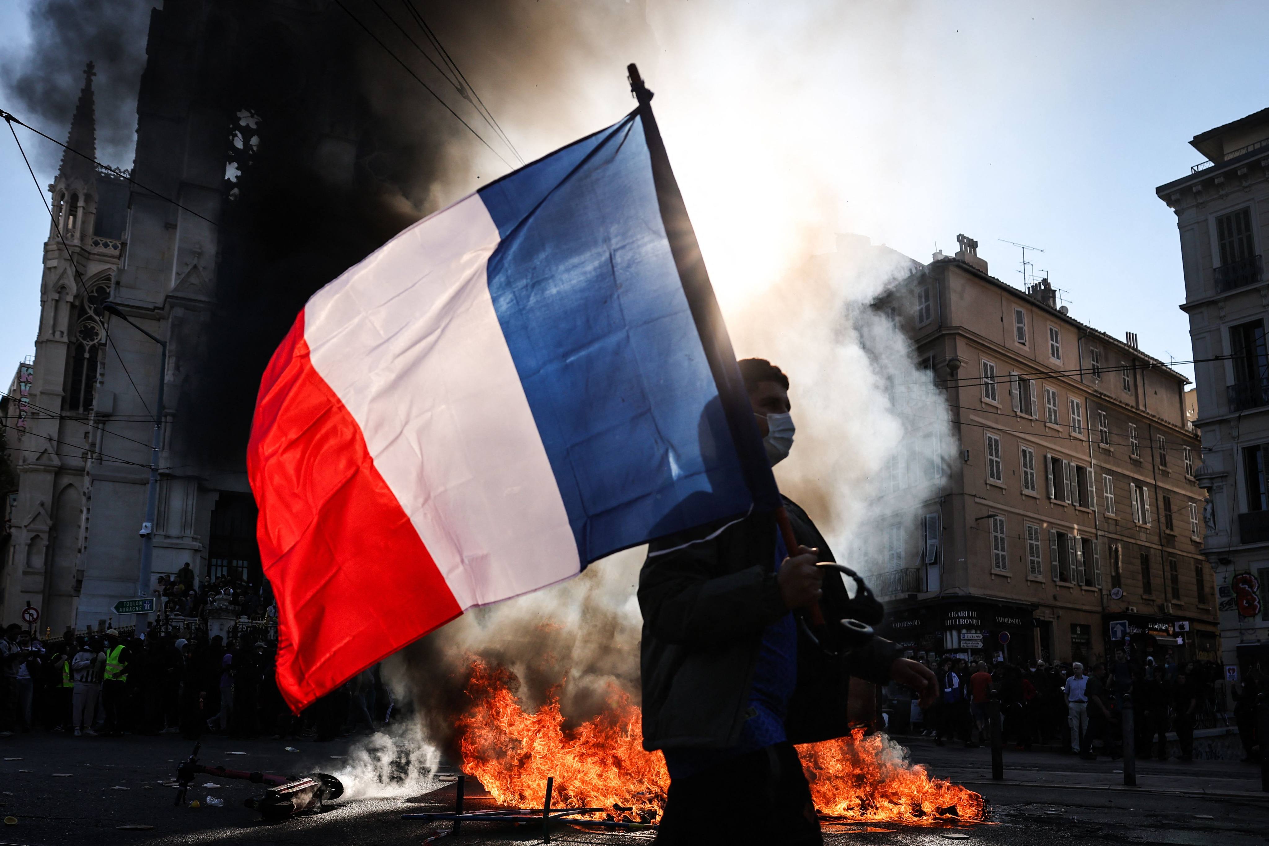 A protester waving a French national flag walks past a fire during clashes. Photo: AFP