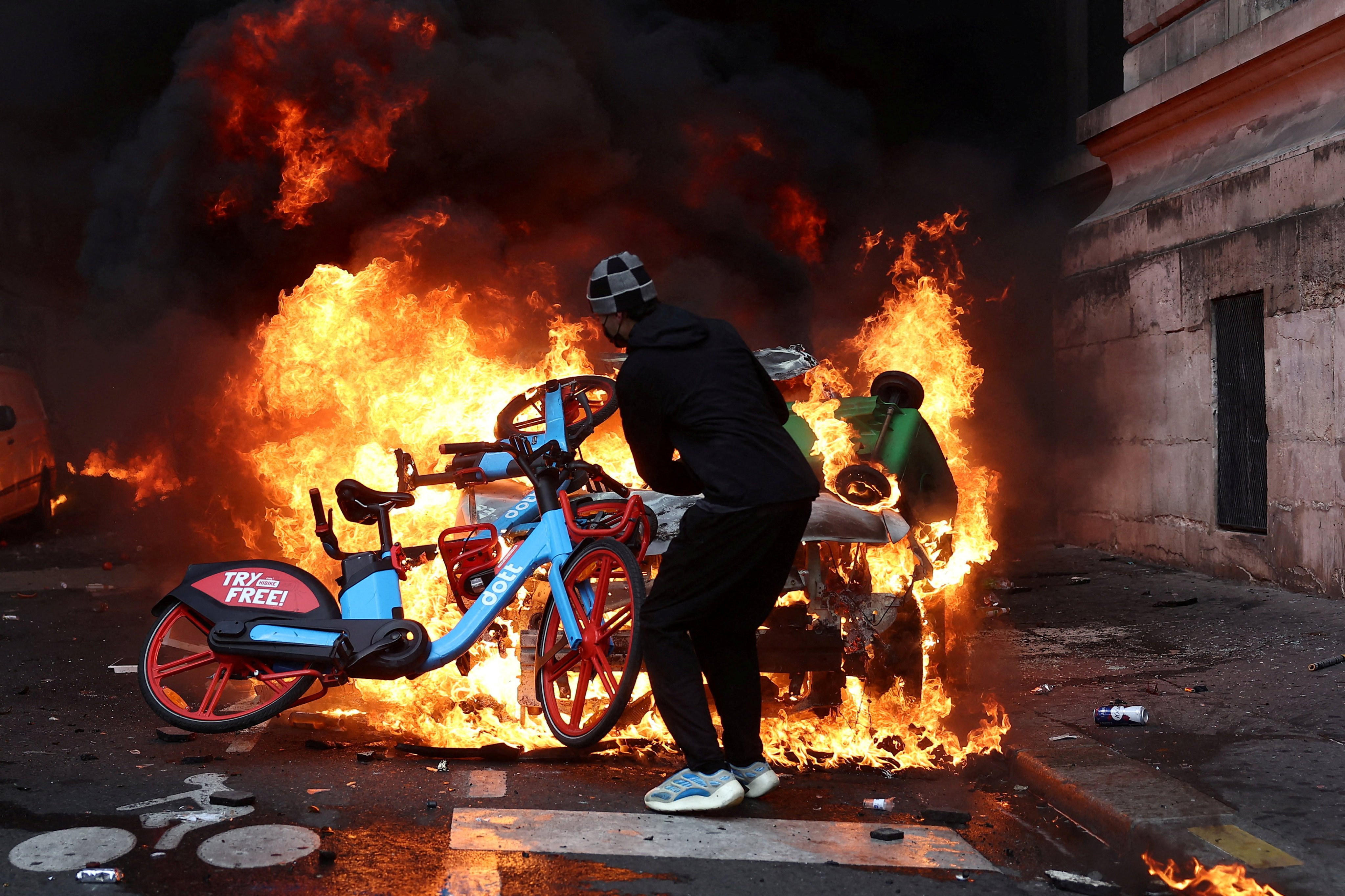 A protester throws a bicycle onto a burning car in Paris on Saturday. Photo: Reuters