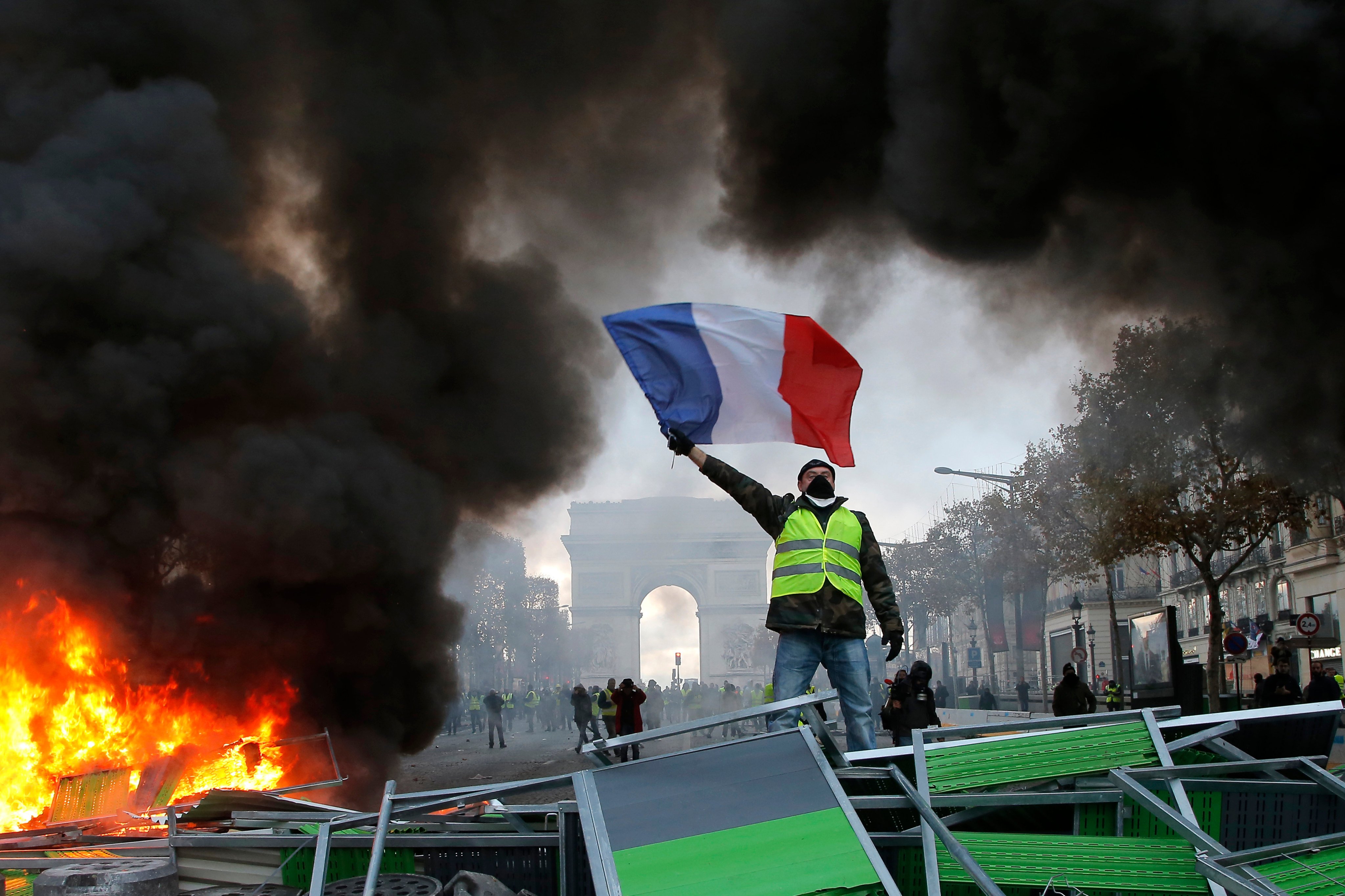 A ‘yellow vest’ demonstrator waves the French flag atop a barricade on the Champs-Elysees with the Arc de Triomphe in the background in November 2018. Photo: AP