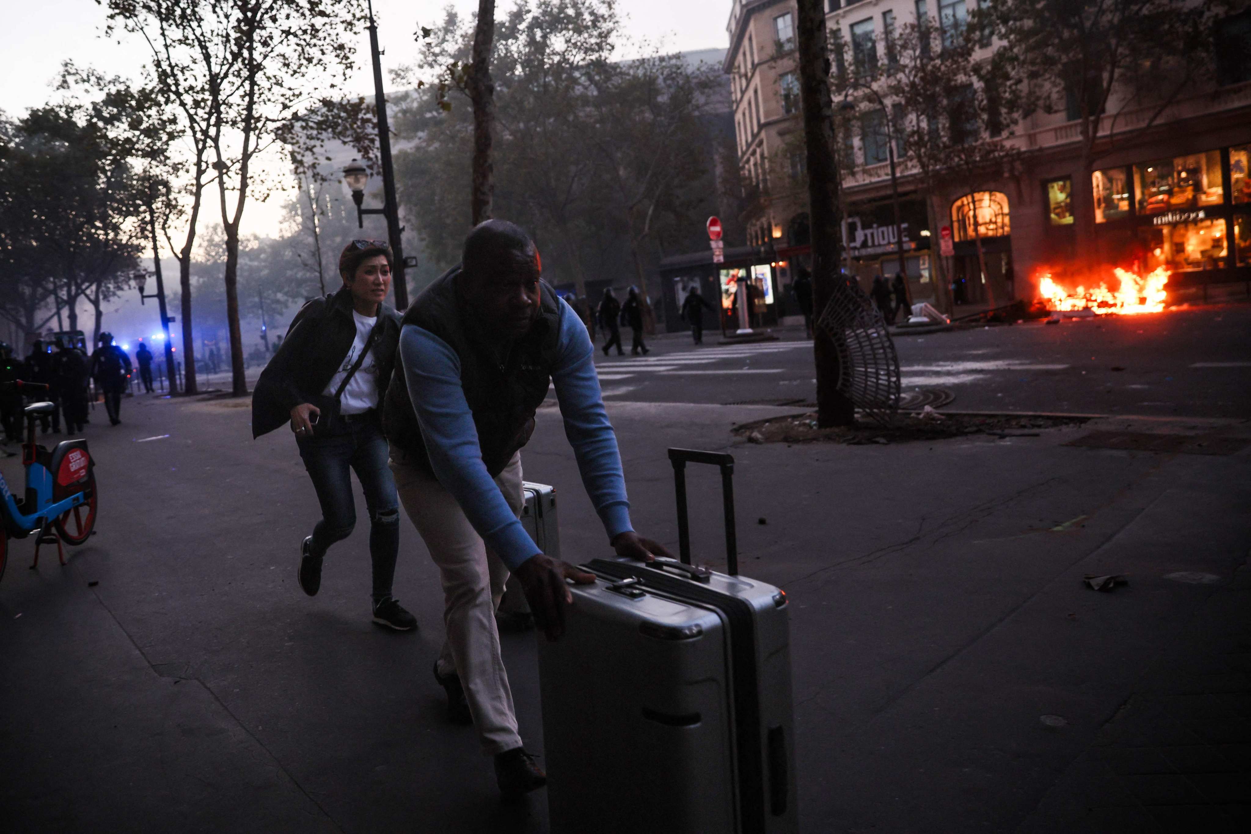 Tourists run with their luggage near a fire during a protest against the high cost of living in Paris on Saturday. Photo: AFP