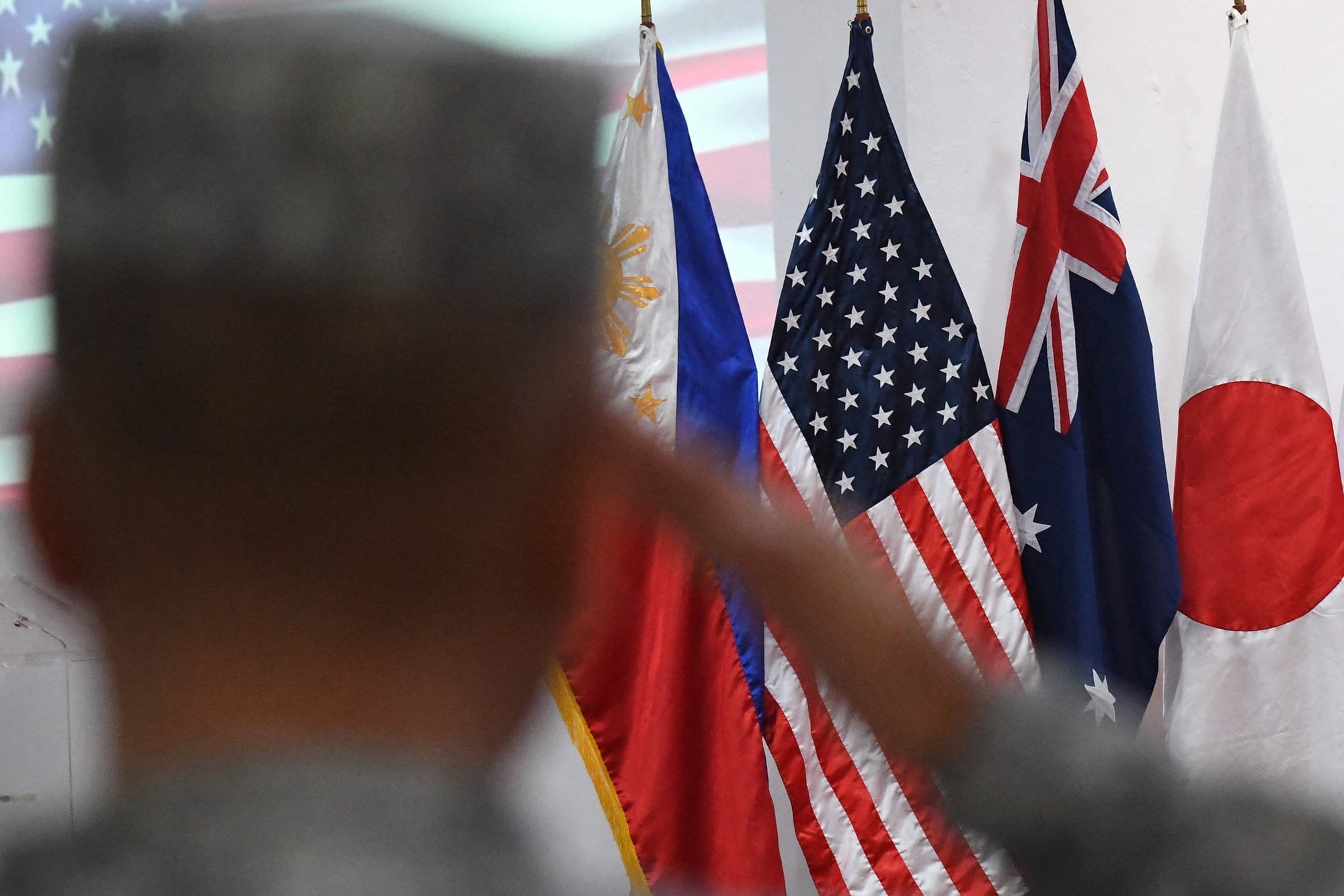 A Filipino marine salutes in front of US, Philippine, Australian, Japanese and South Korean flags during the opening ceremony of a joint military exercise in October 2024. Photo: AFP