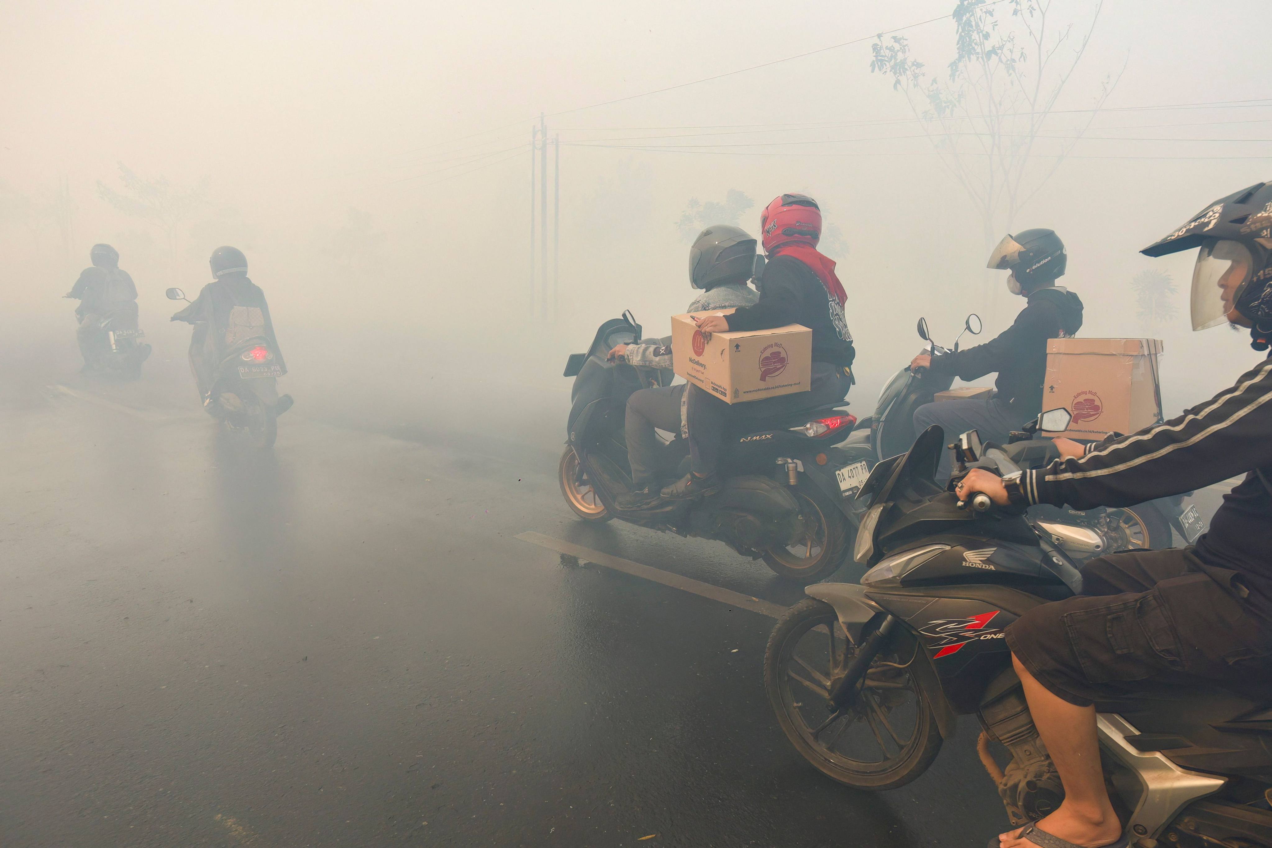 Motorcyclists ride along a road heavily obscured by thick haze from nearby wildfires in South Kalimantan, Indonesia, on Tuesday. Photo: AFP