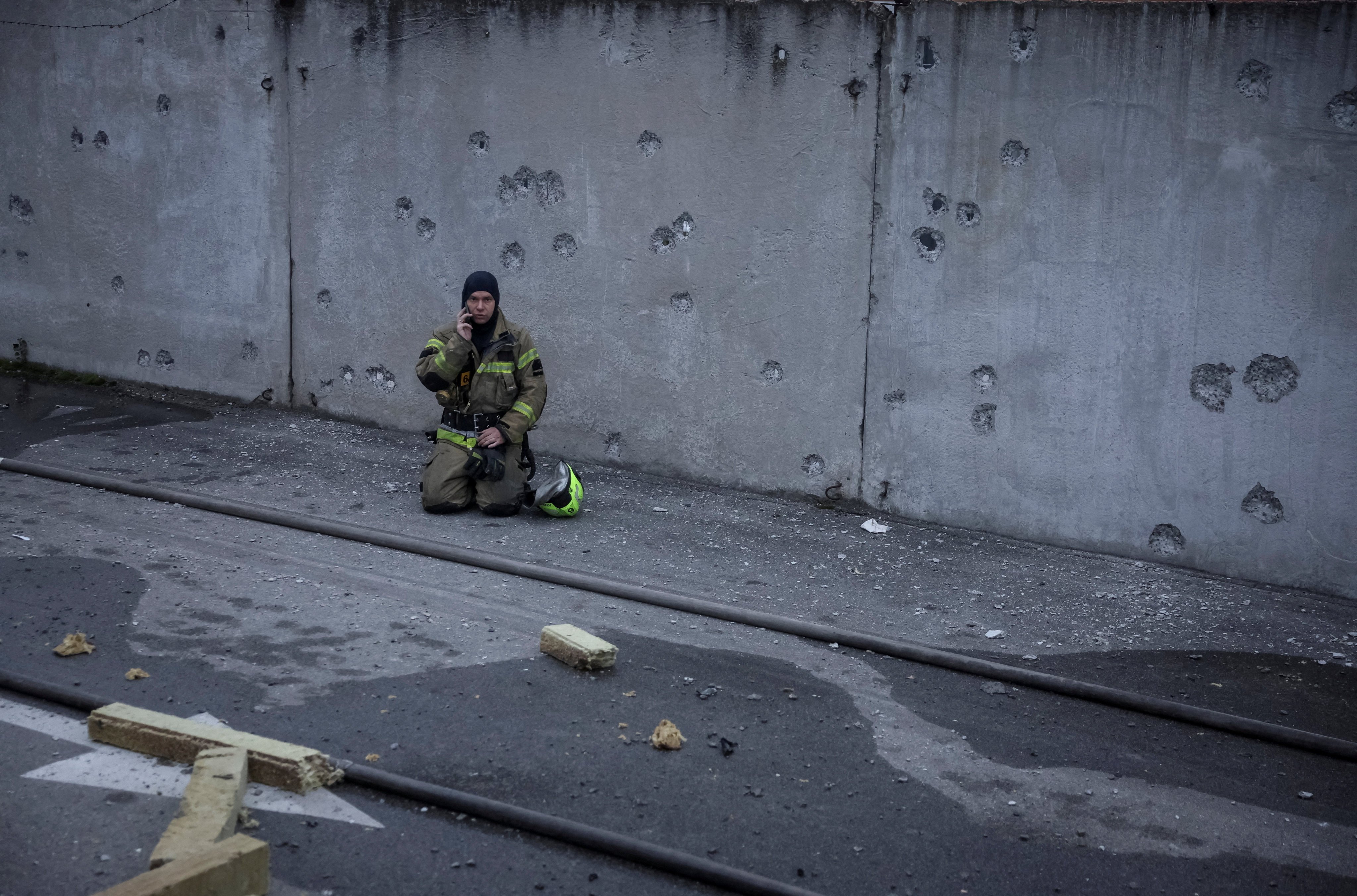 A rescuer takes a break near a wall with shrapnel holes in Kyiv. Photo: Reuters