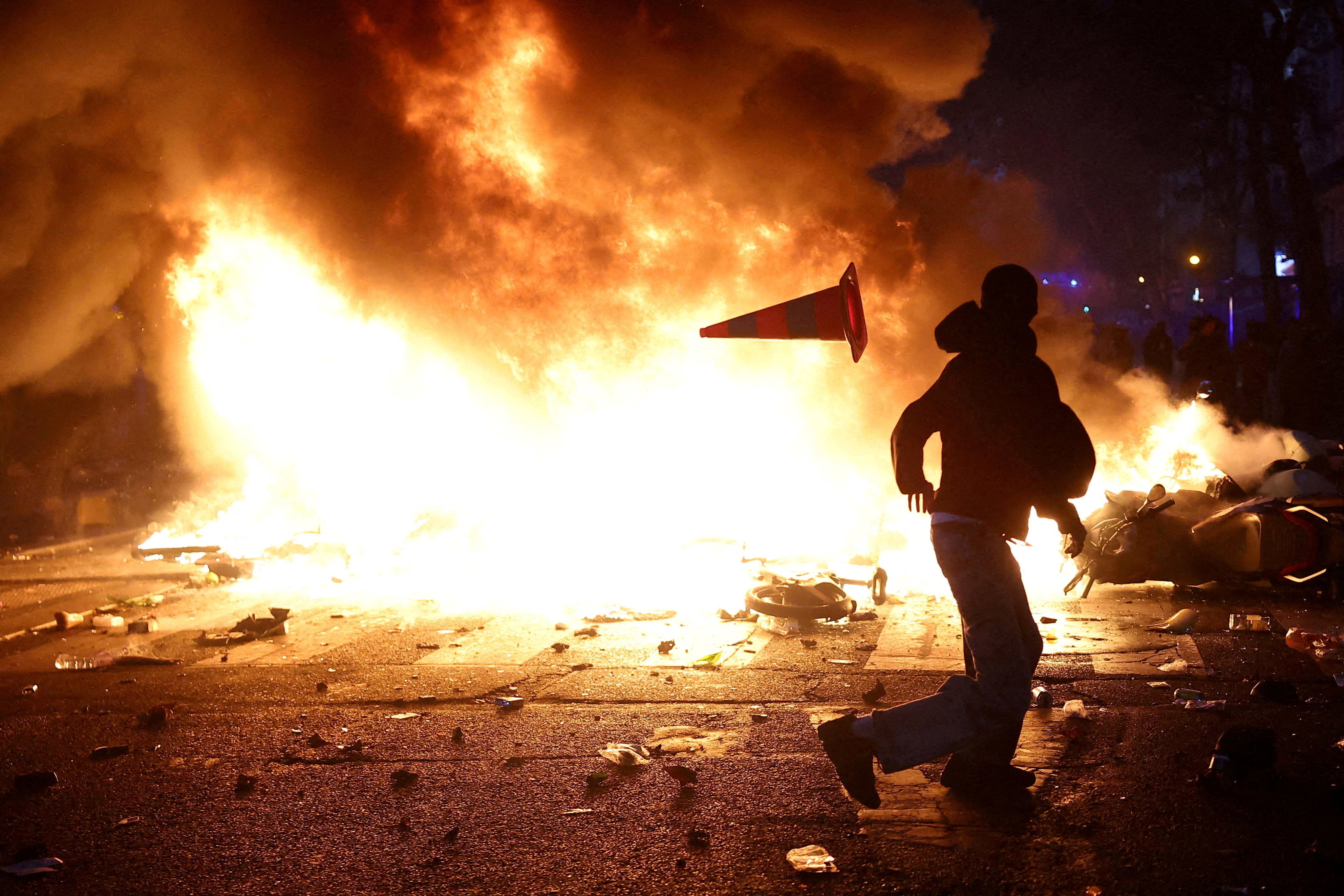 A man throws a plastic traffic cone through a burning barricade amid clashes during a day of demonstrations in Paris on October 17. Photo: Reuters