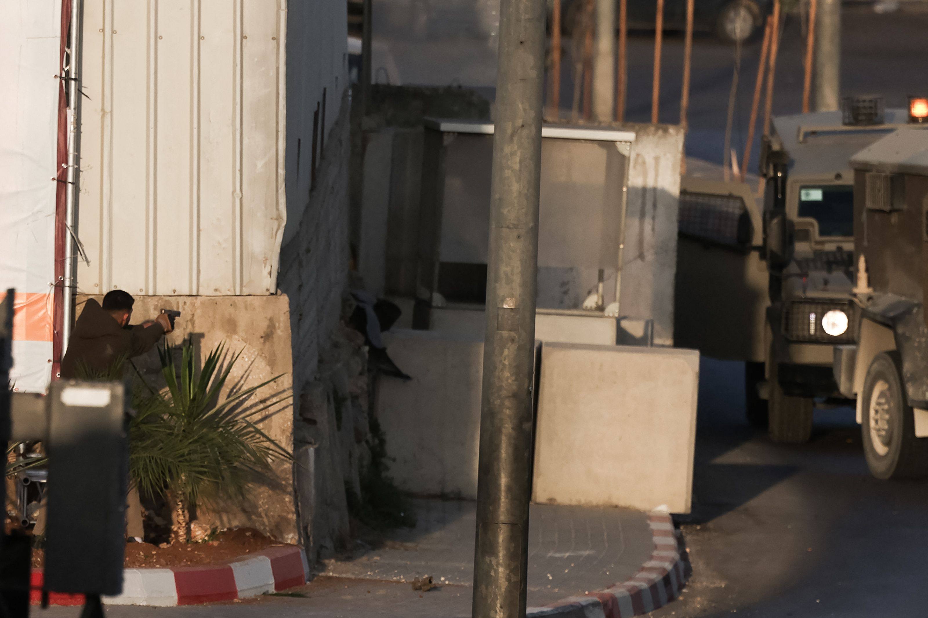 A Palestinian gunman aims a handgun towards Israeli military vehicles. Photo: AFP