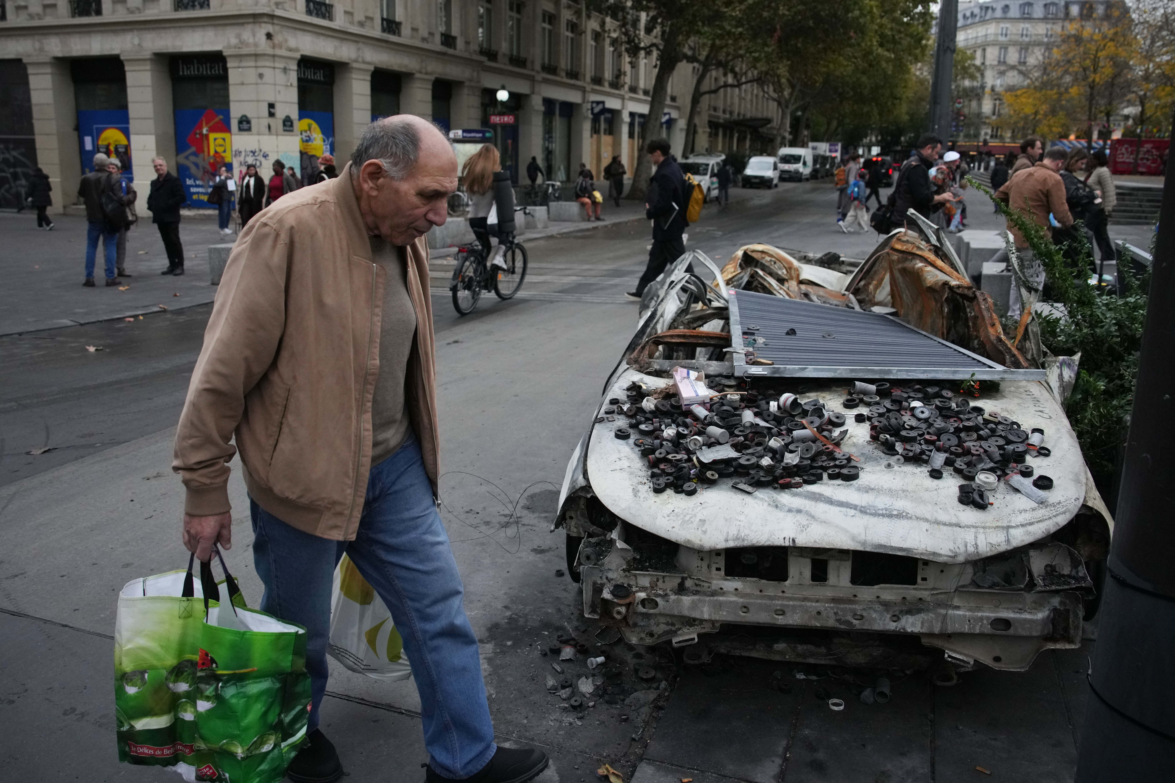 A man walks past a burned-out car in Paris, France, on Tuesday following protests against the high cost of living. Photo: AP