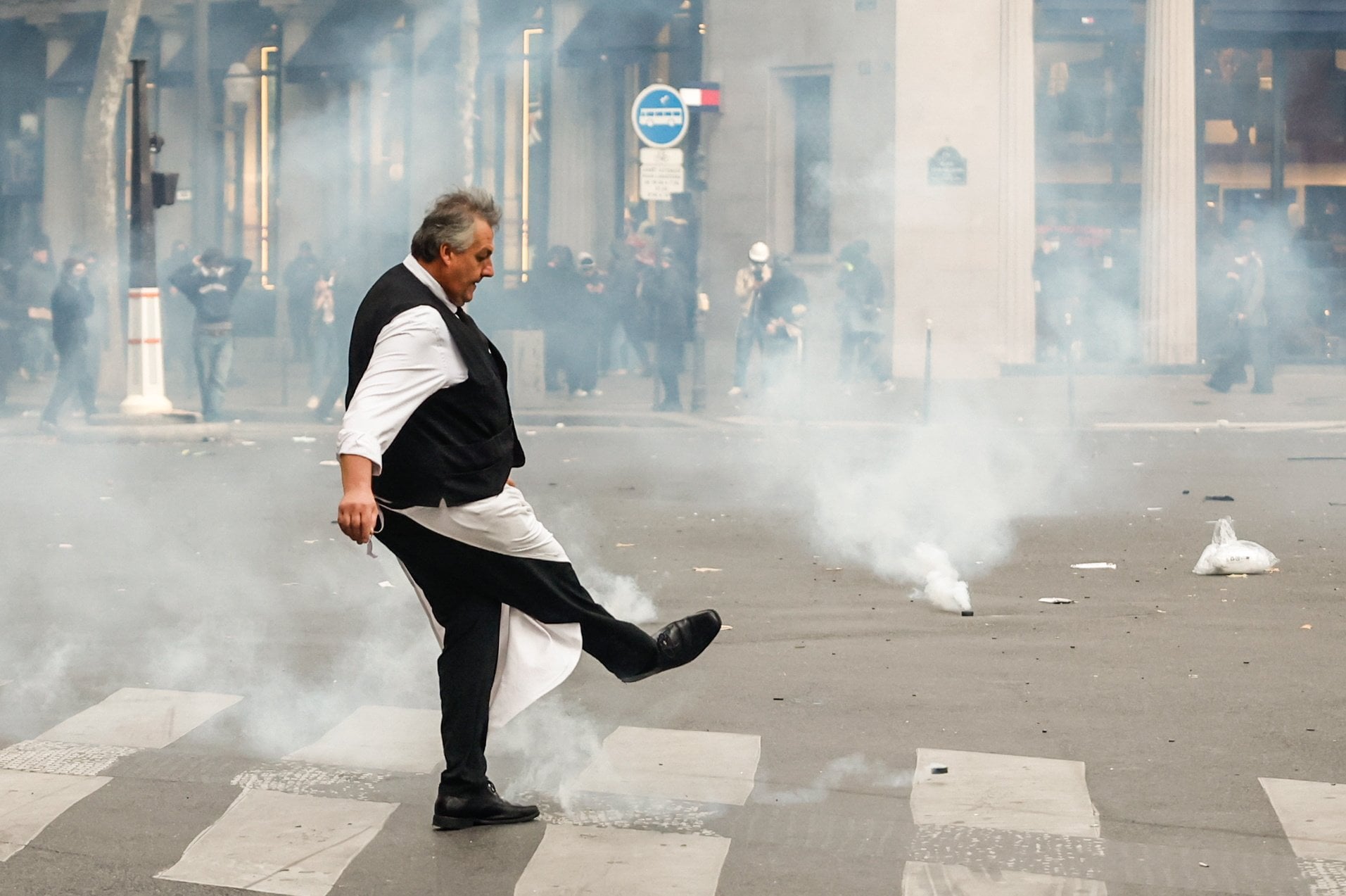 A cafe waiter tries to push back tear gas canisters during clashes between protesters and police in Paris on Saturday. Photo: EPA