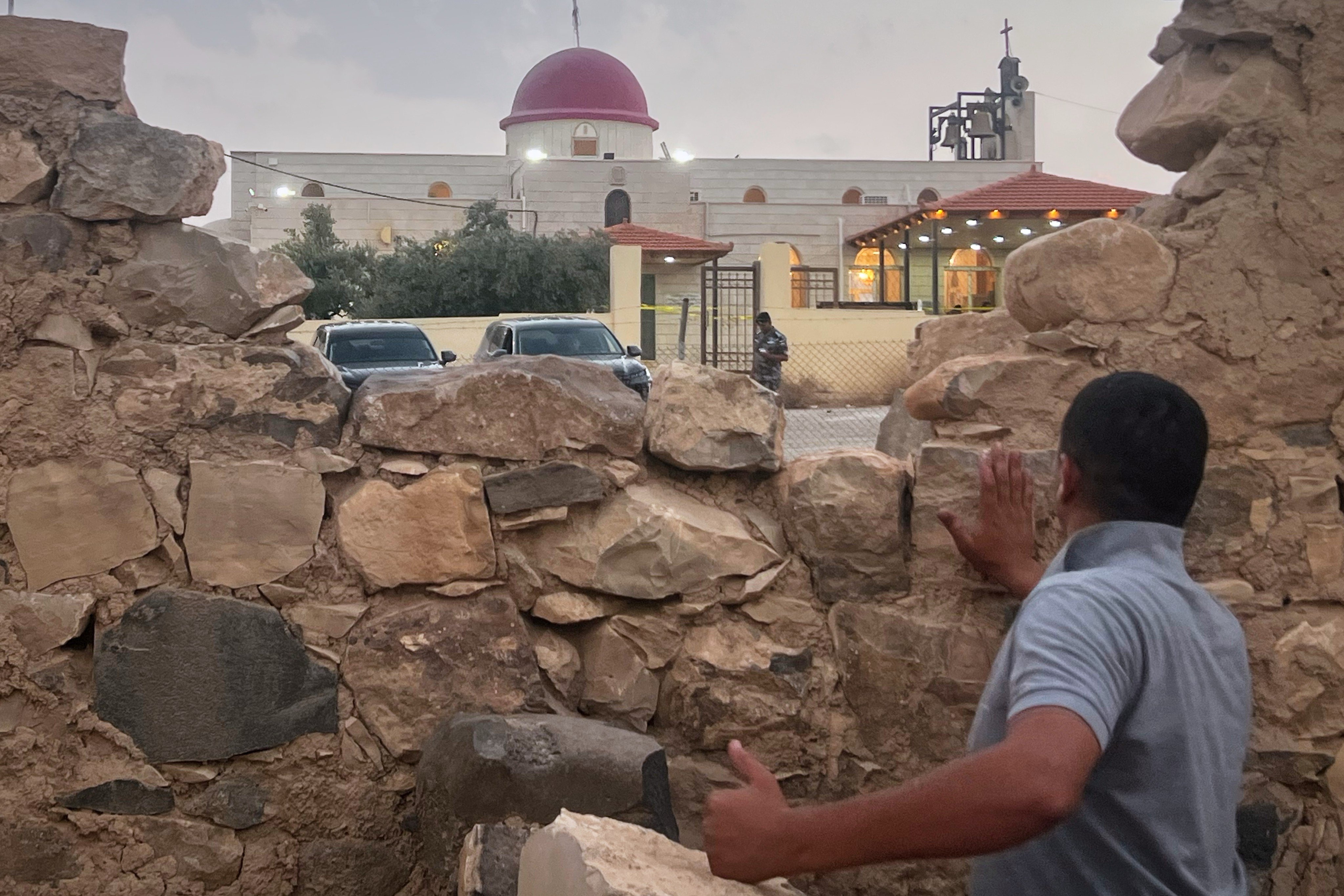 A man looks through a gap in a stone wall toward a Greek Orthodox church where gunmen opened fire during a funeral on Friday. Photo: AP