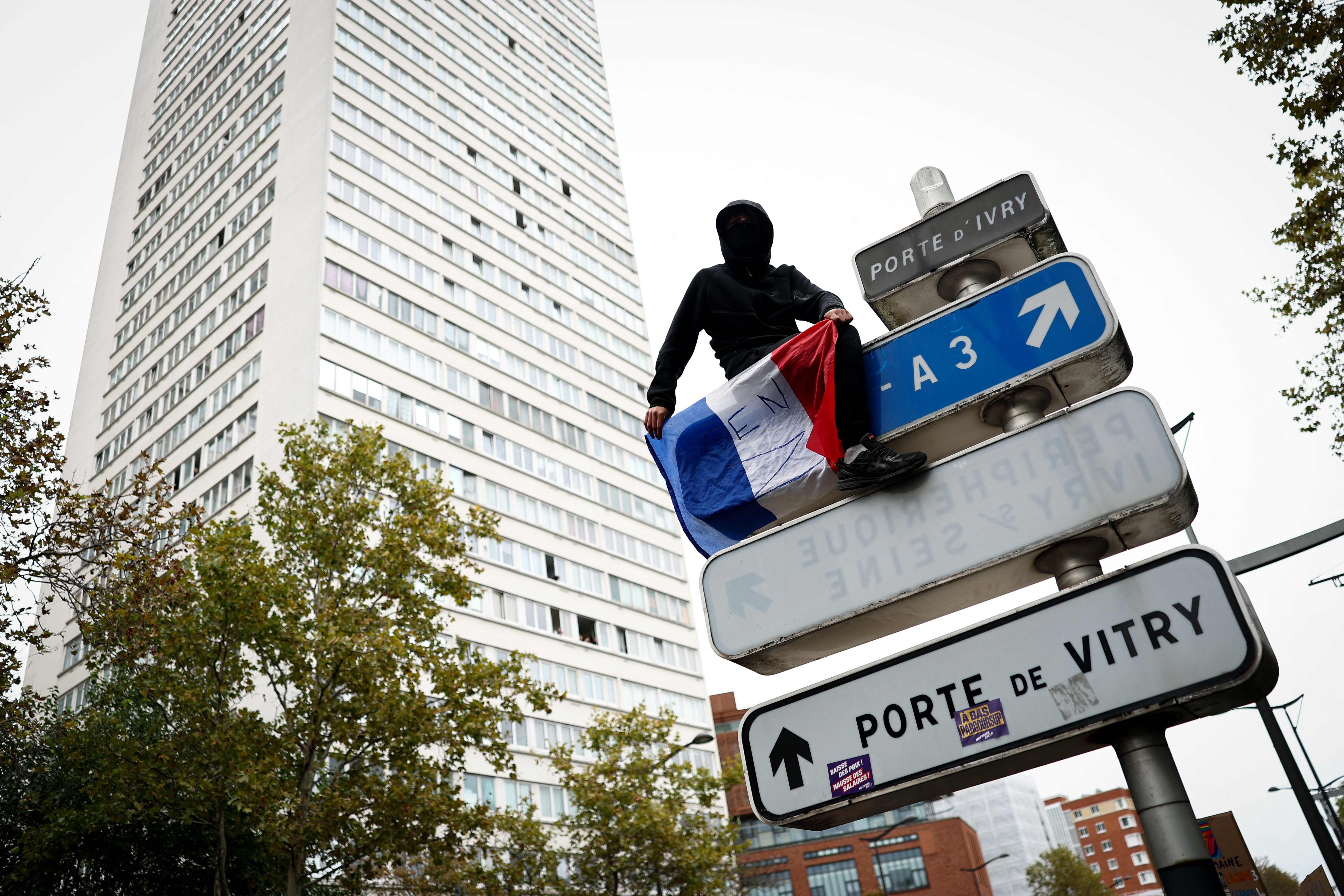 A protester sits atop a public road sign in Paris. Photo: AFP