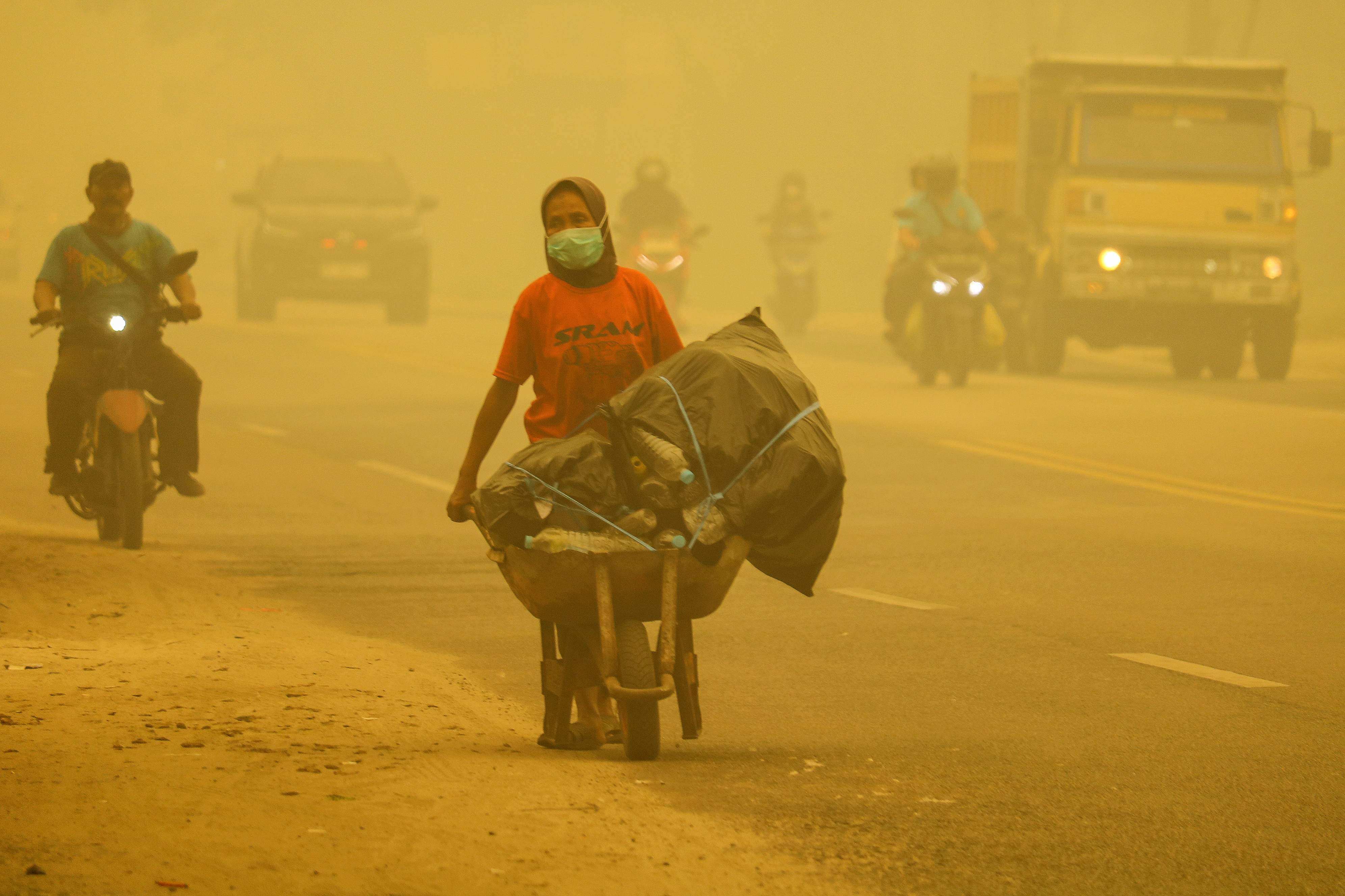 A woman wearing a face mask pushes a cart along a road amid thick haze from forest and land fires in the region in Palangkaraya, Central Kalimantan, on Sunday. Photo: AFP