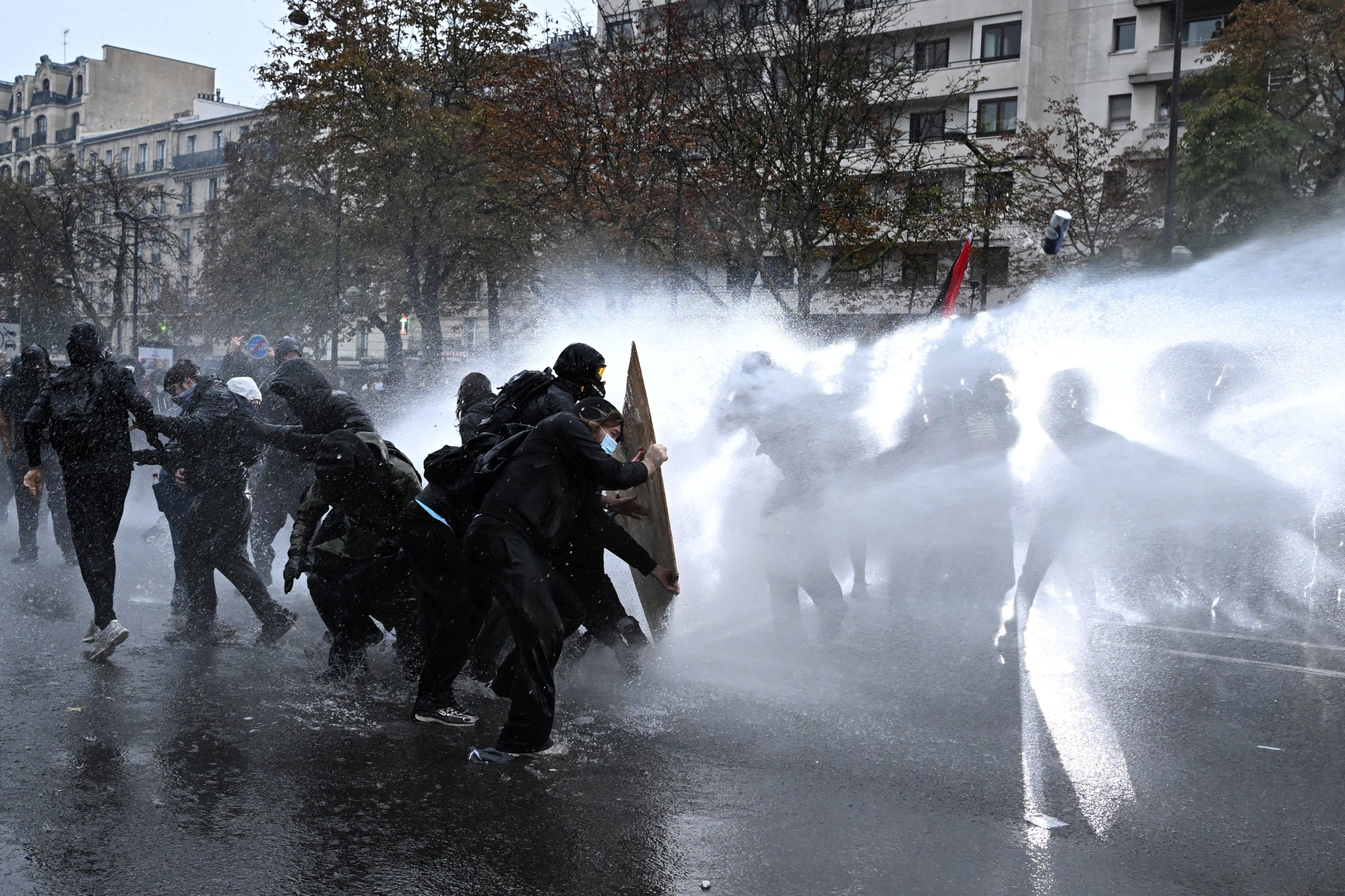 Protesters take cover behind a plywood board as French riot police use a water canon amid clashes in France on October 24. Photo: Reuters
